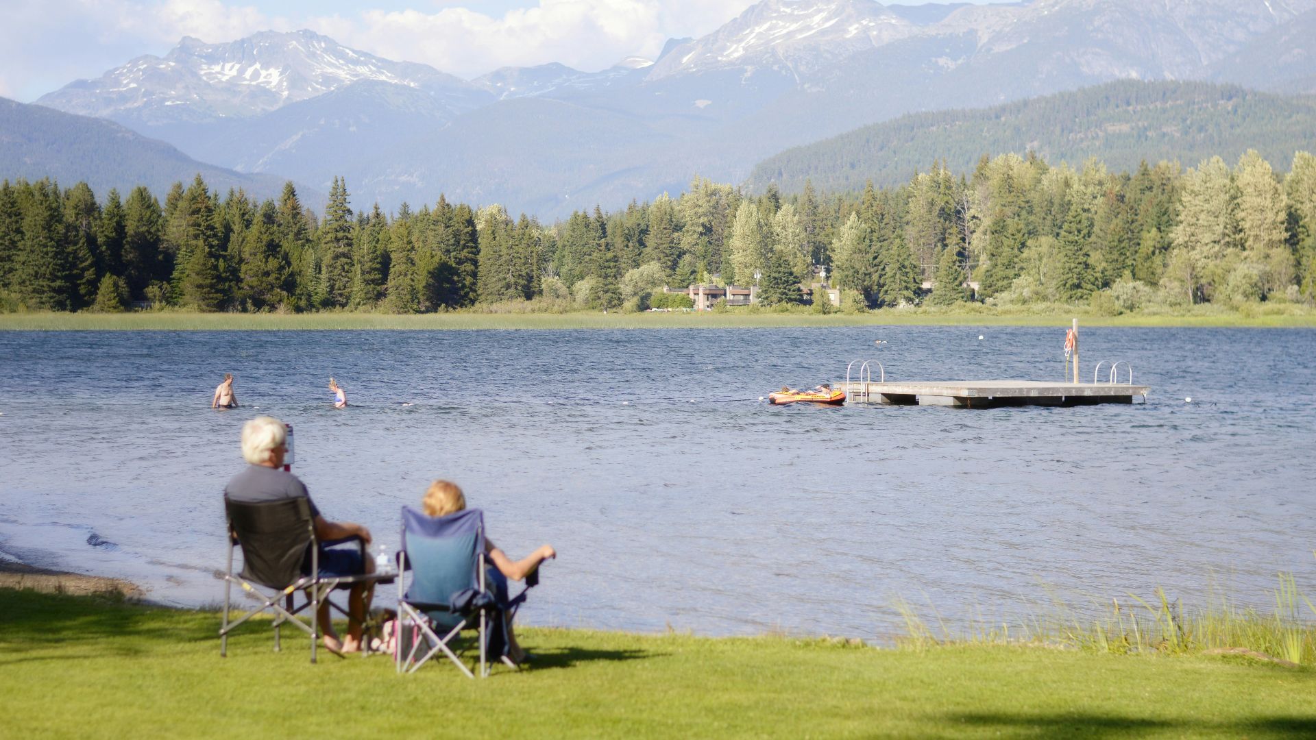 two persons sitting on grass facing the lake