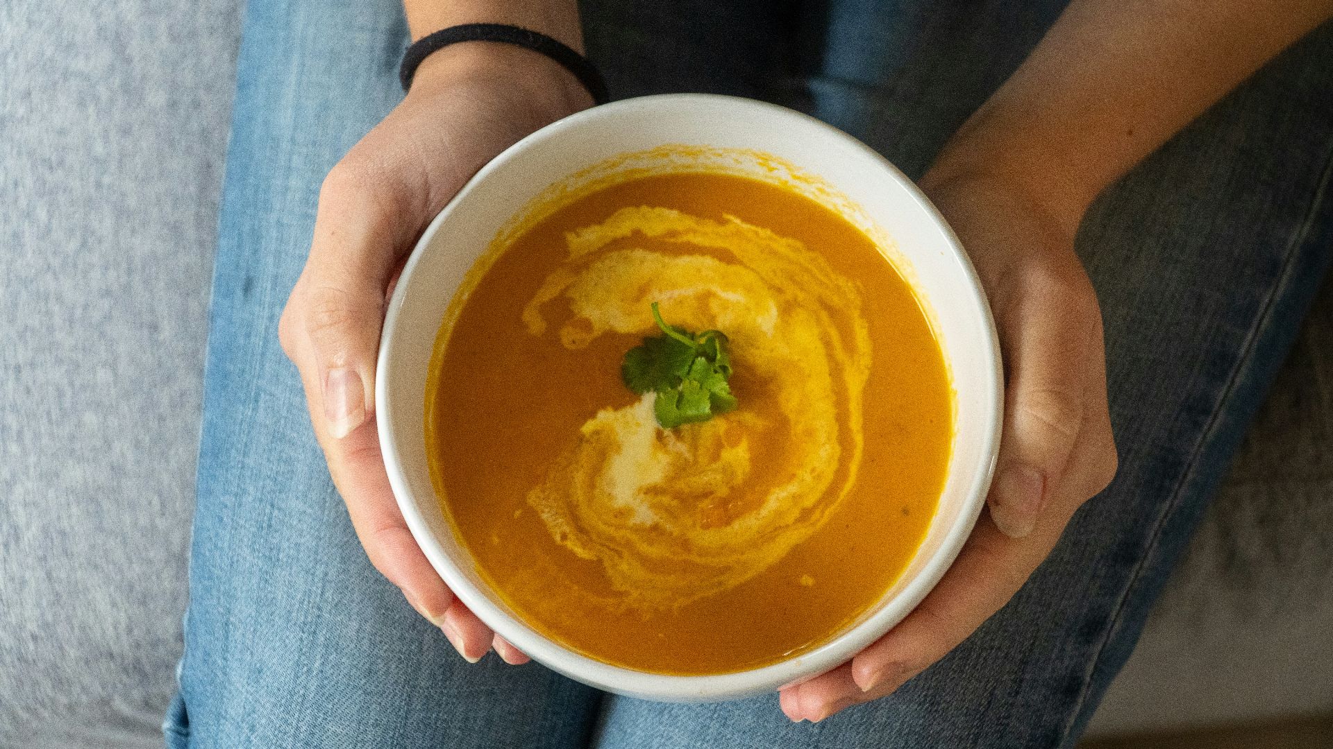 Bowl of creamy orange soup with swirl and herb garnish