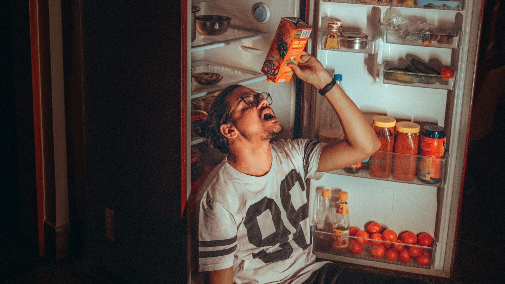 boy in white and black tank top standing beside red top mount refrigerator