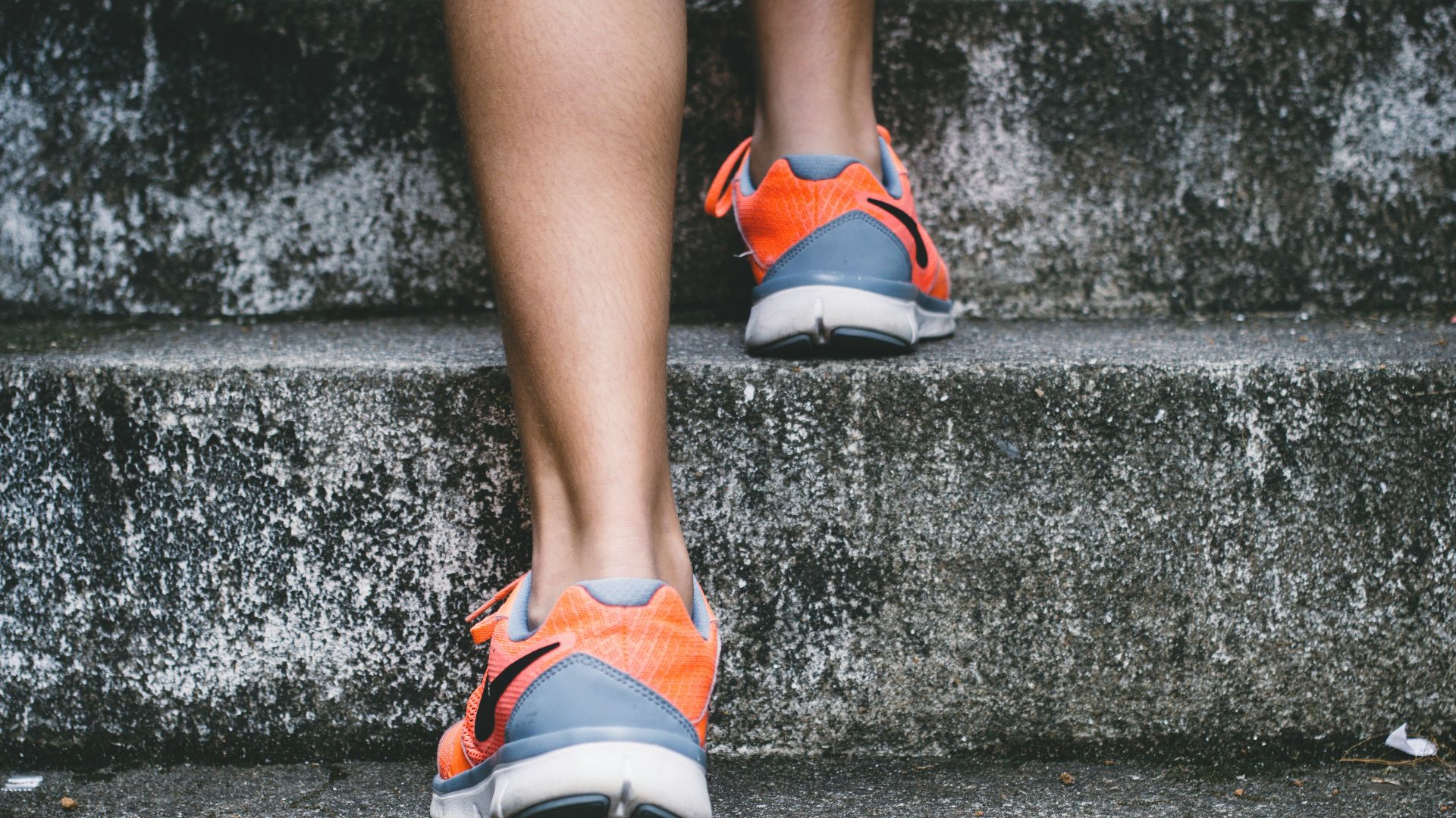 person wearing orange and gray Nike shoes walking on gray concrete stairs