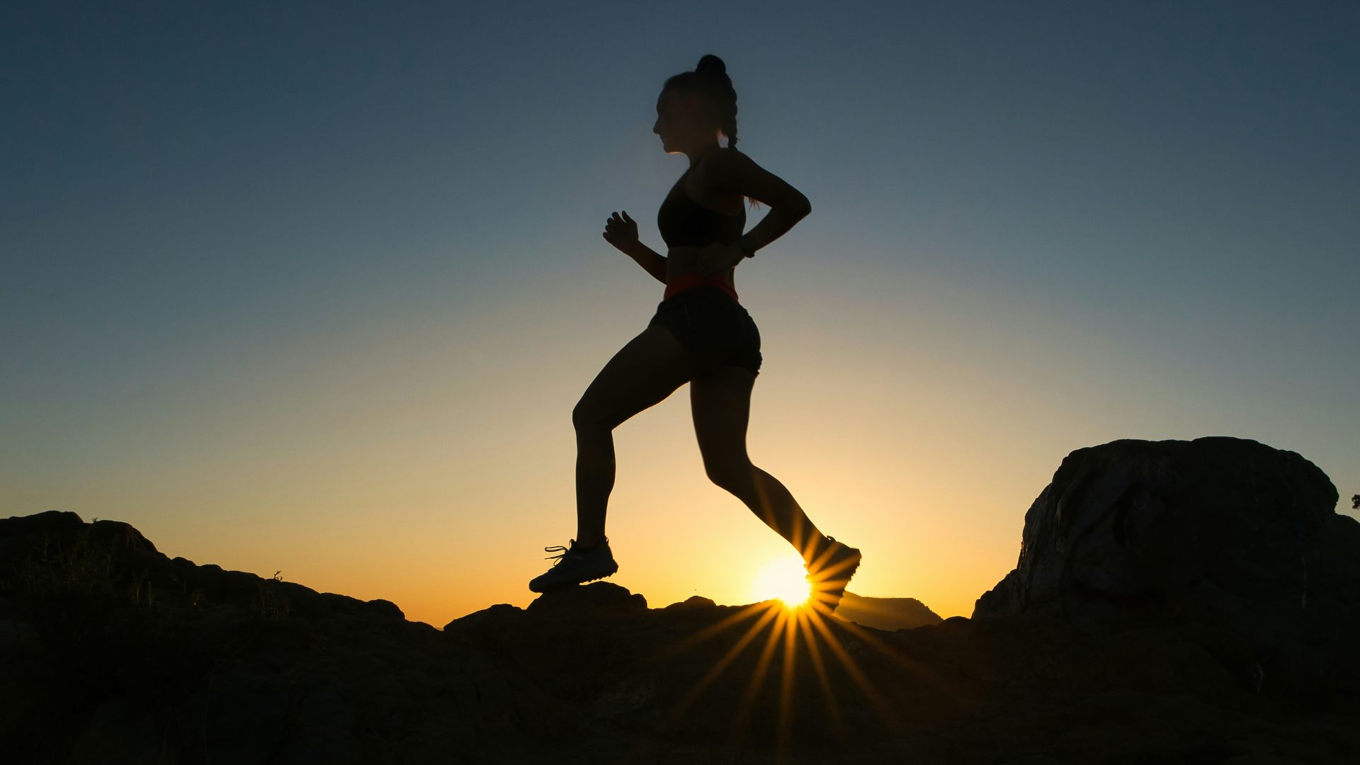 silhouette of man jumping on rocky mountain during sunset