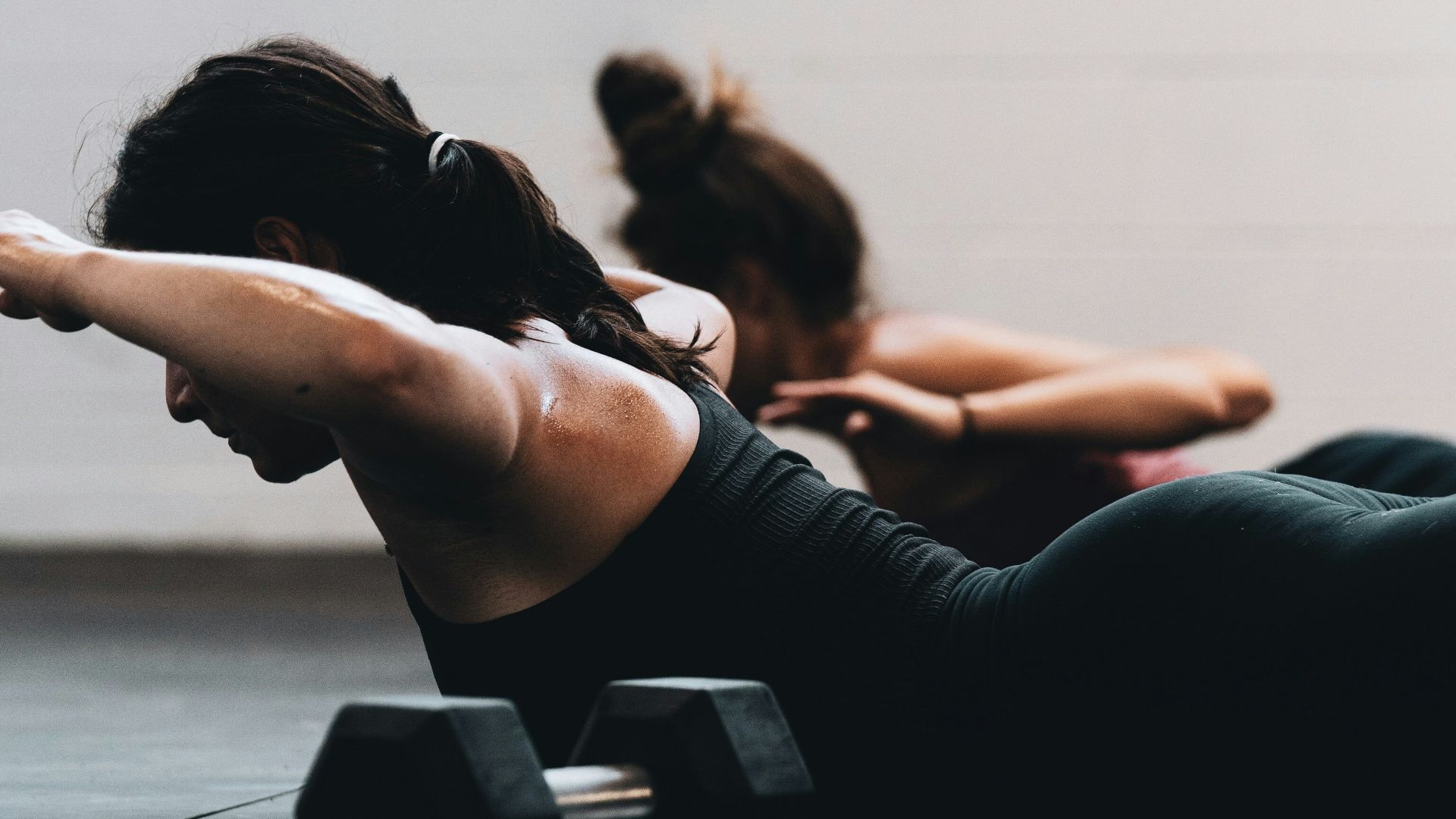 woman in black tank top and black leggings lying on black floor