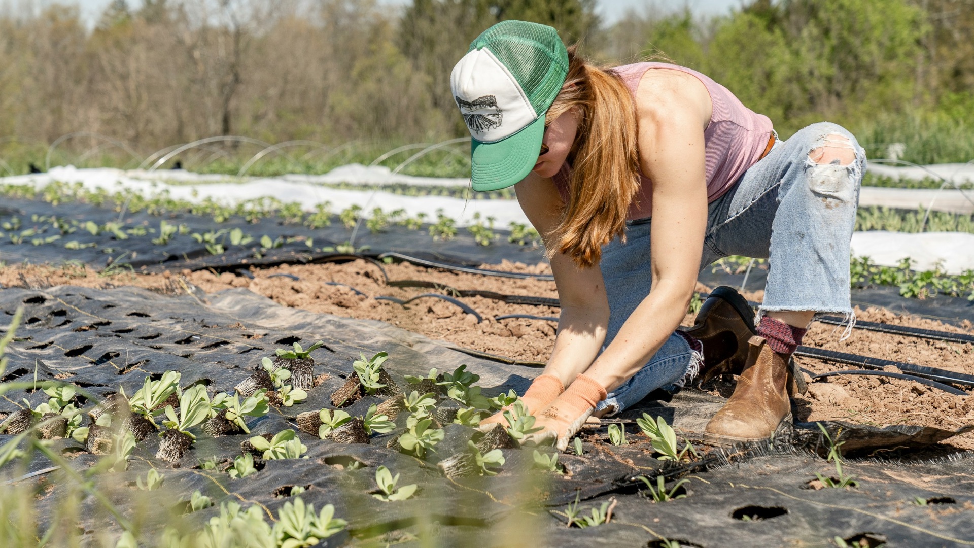 woman in pink shirt and blue denim jeans sitting on brown rock near river during daytime