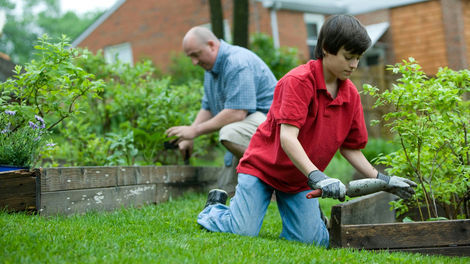 man in red polo shirt and blue denim jeans sitting on brown wooden bench during daytime