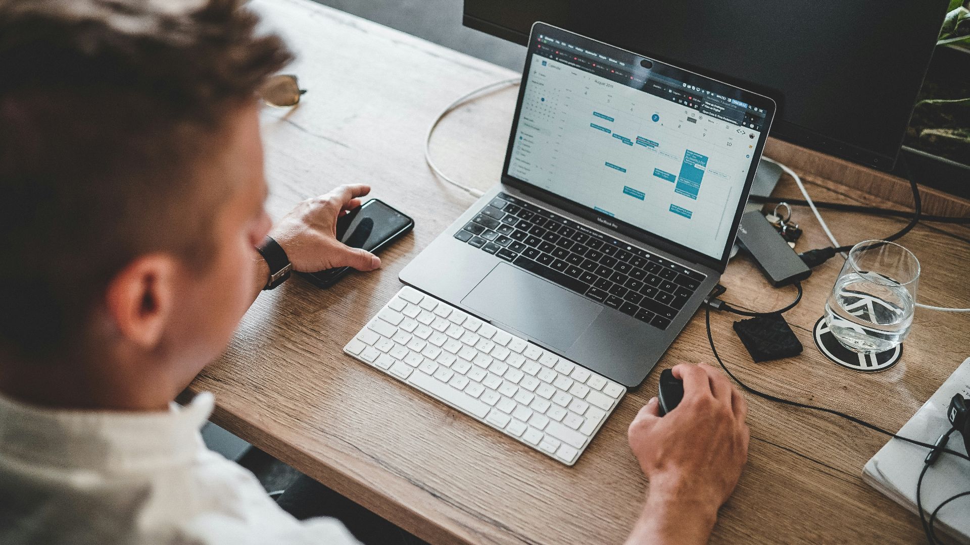 man holding mouse and iPhone while using Macbook Pro
