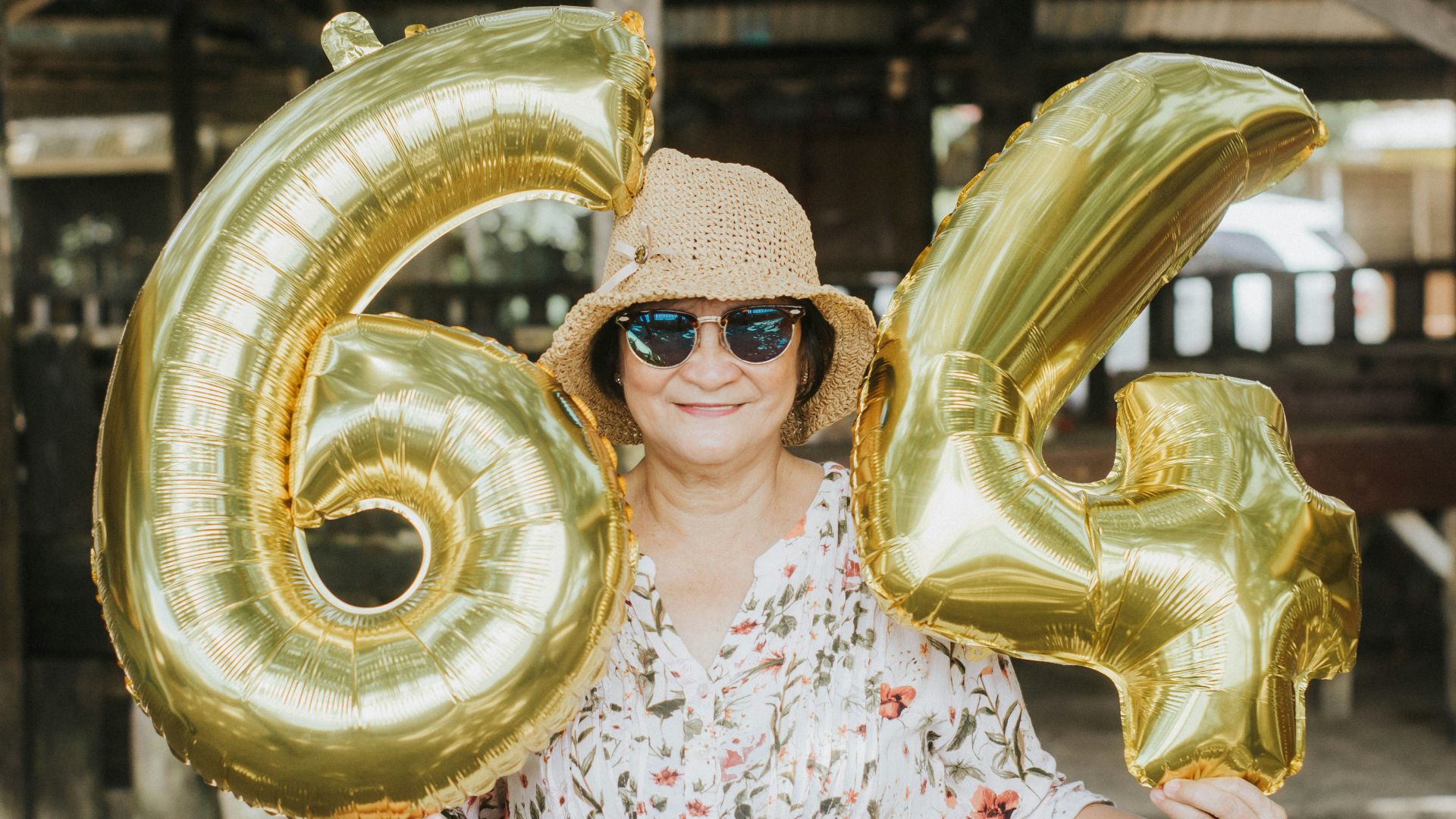 a woman in a hat and sunglasses holding up large gold balloons