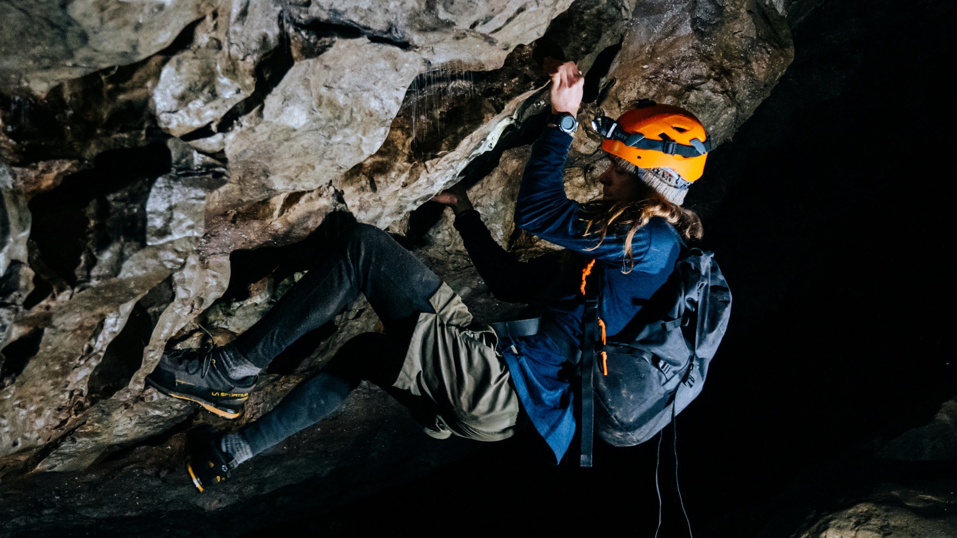 man in blue jacket and black pants sitting on rock