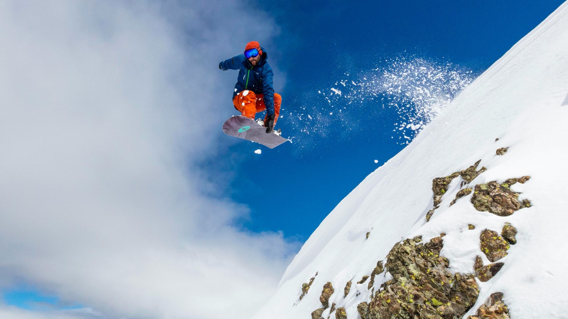 man in red jacket and blue pants sitting on snow covered mountain during daytime
