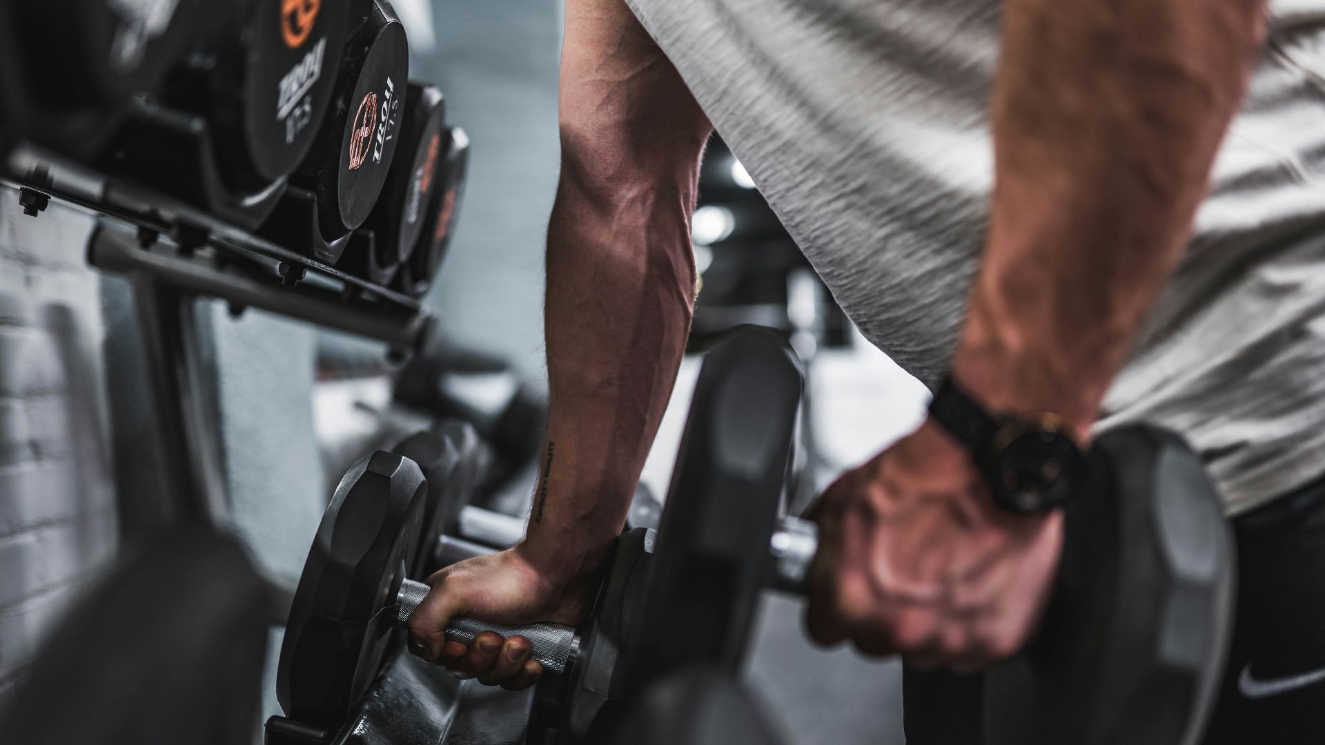person in gray shirt holding black dumbbell