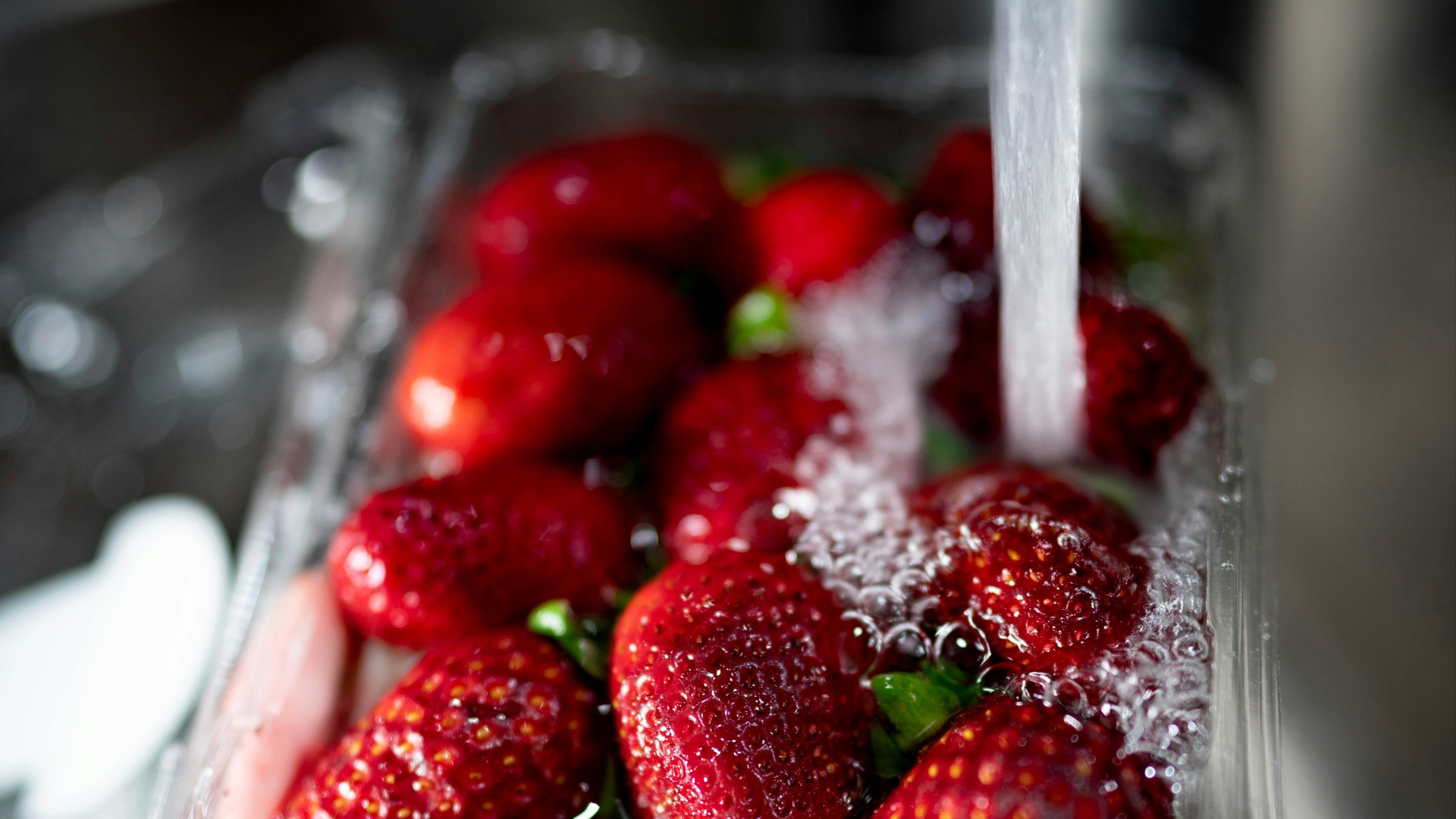 water poured into red strawberries in plastic tray