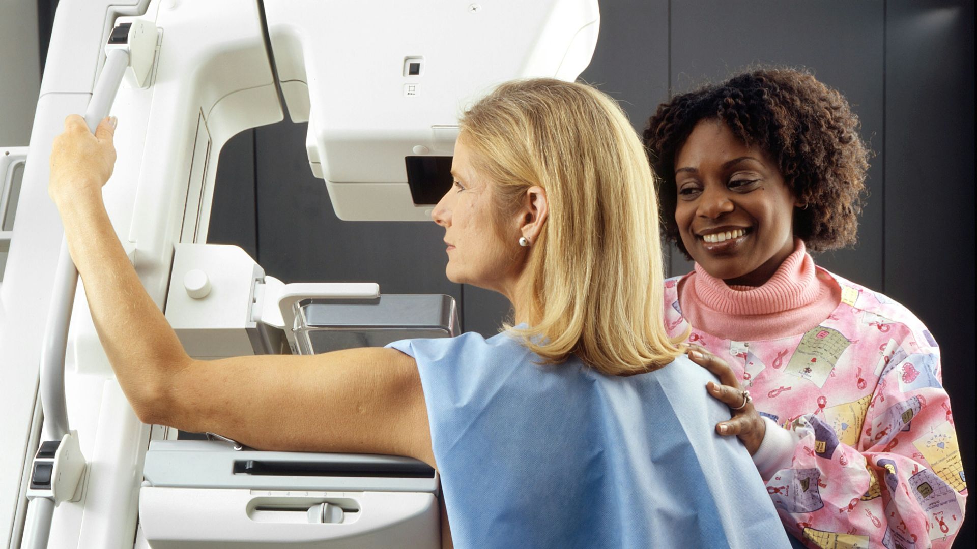 smiling woman standing near another woman beside mammogram machine