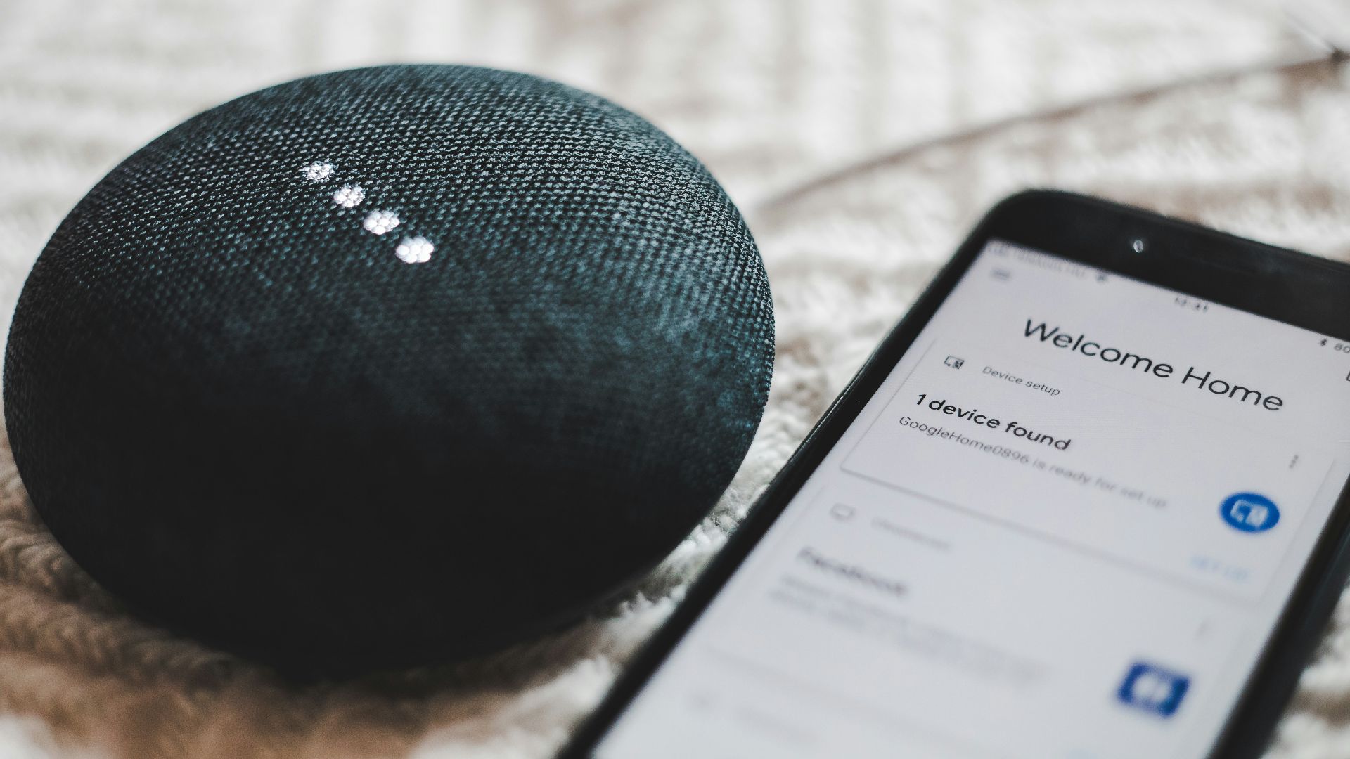 turned-on charcoal Google Home Mini and smartphone