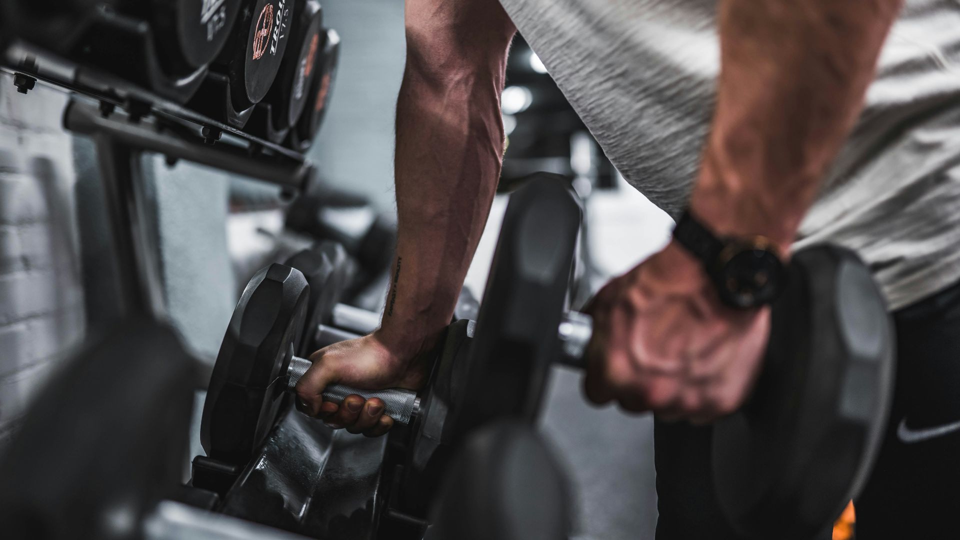 person in gray shirt holding black dumbbell