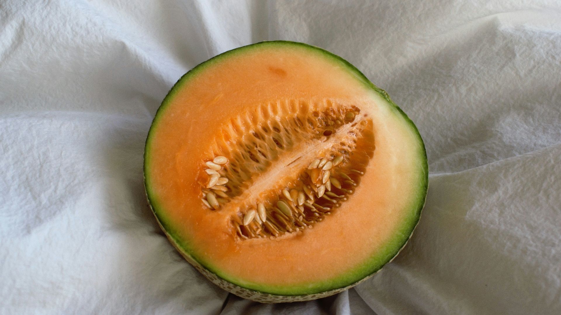 a cut in half melon sitting on top of a white cloth