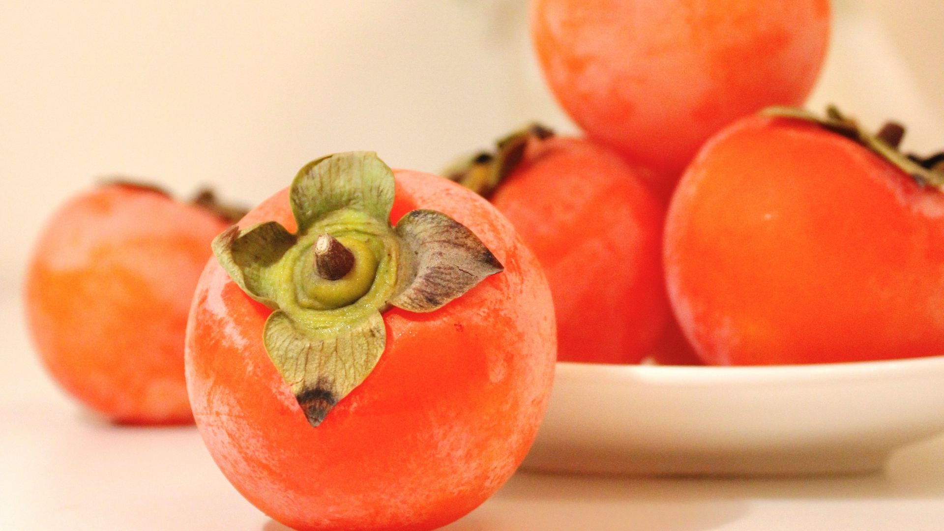 a white plate topped with tomatoes next to a vase of flowers