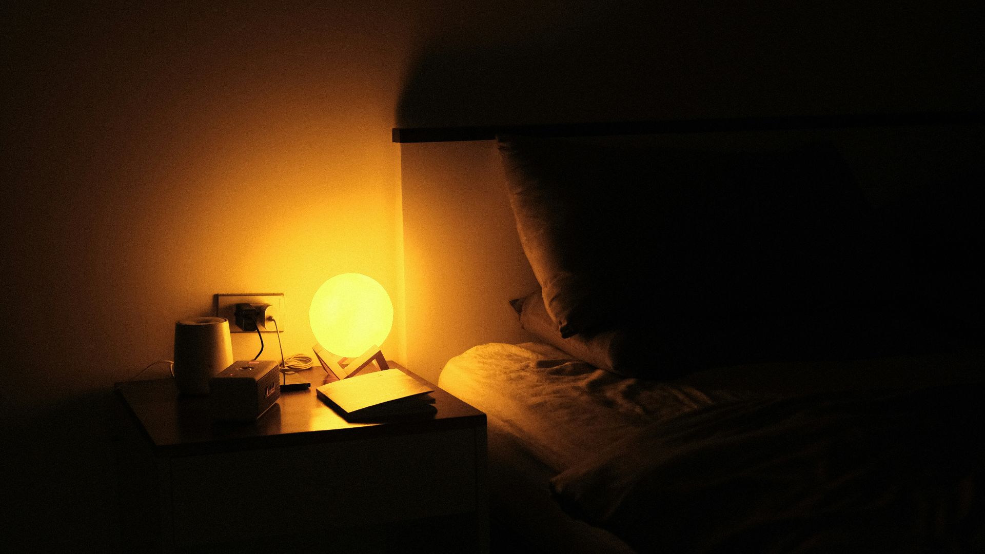 a night stand with a lamp on it next to a bed