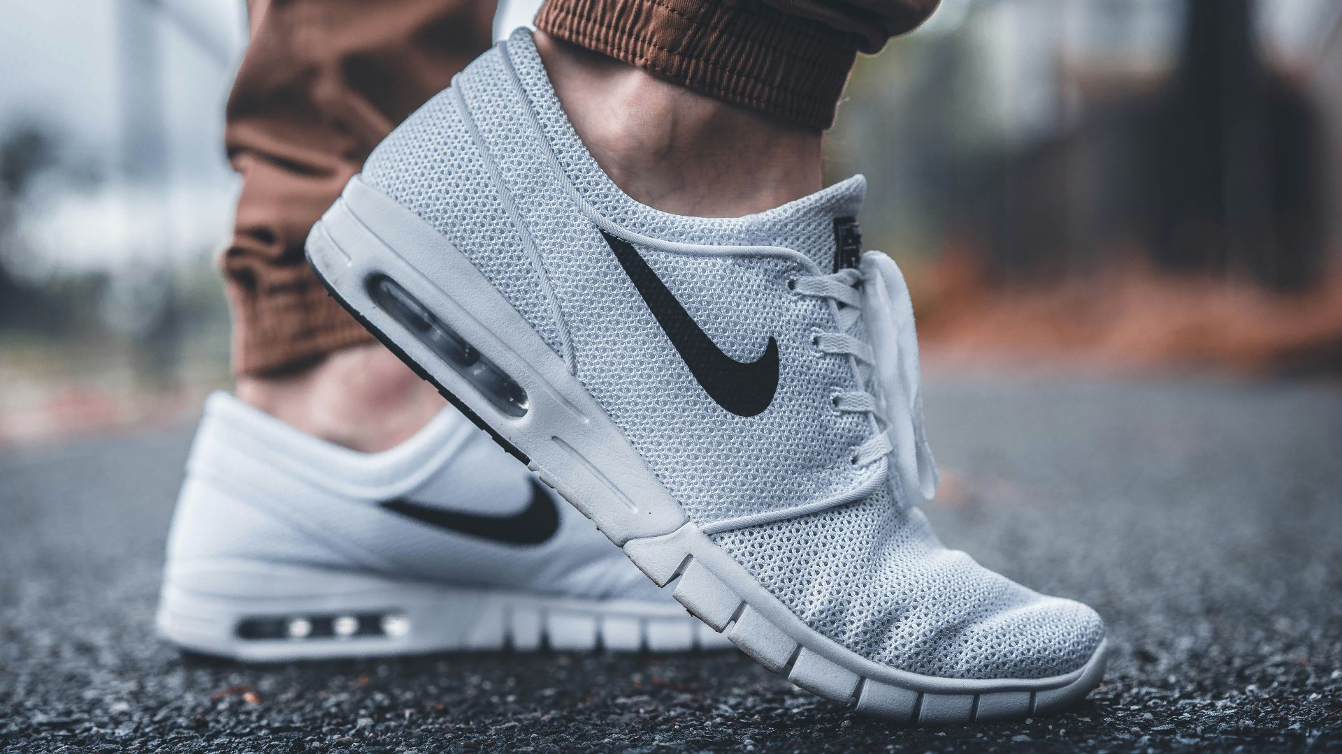 person wearing white Nike running shoes standing on black concrete path