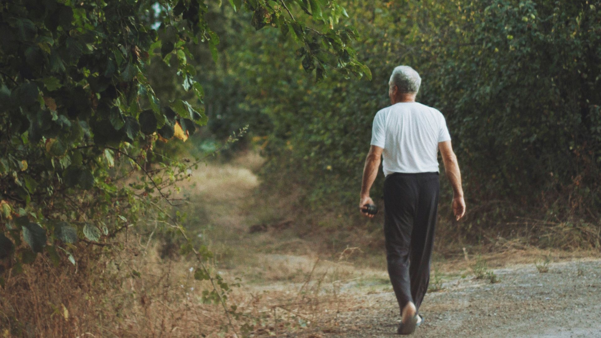 man in white shirt and black pants walking on dirt road