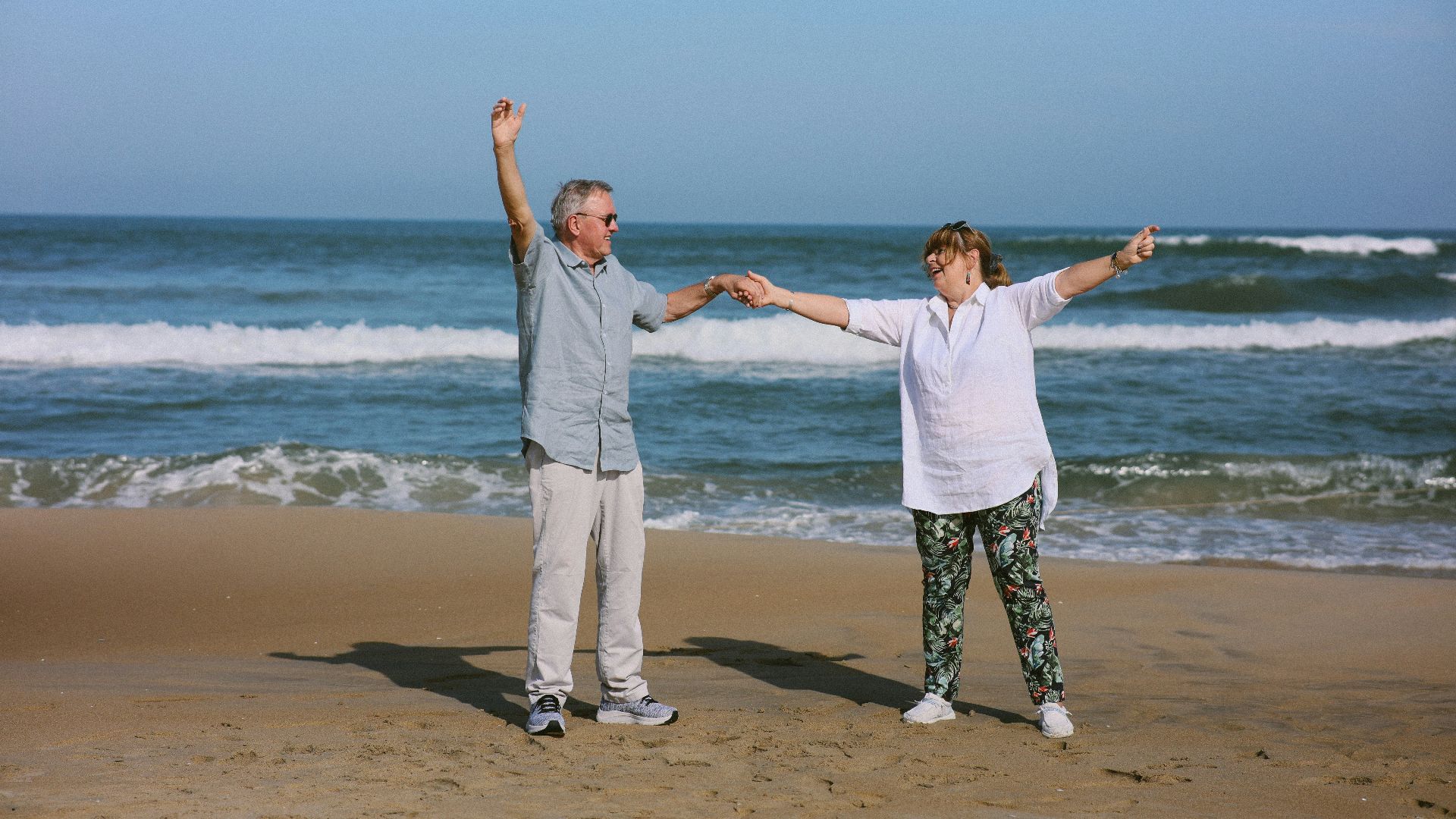 Elderly couple dancing on a beach with ocean waves.