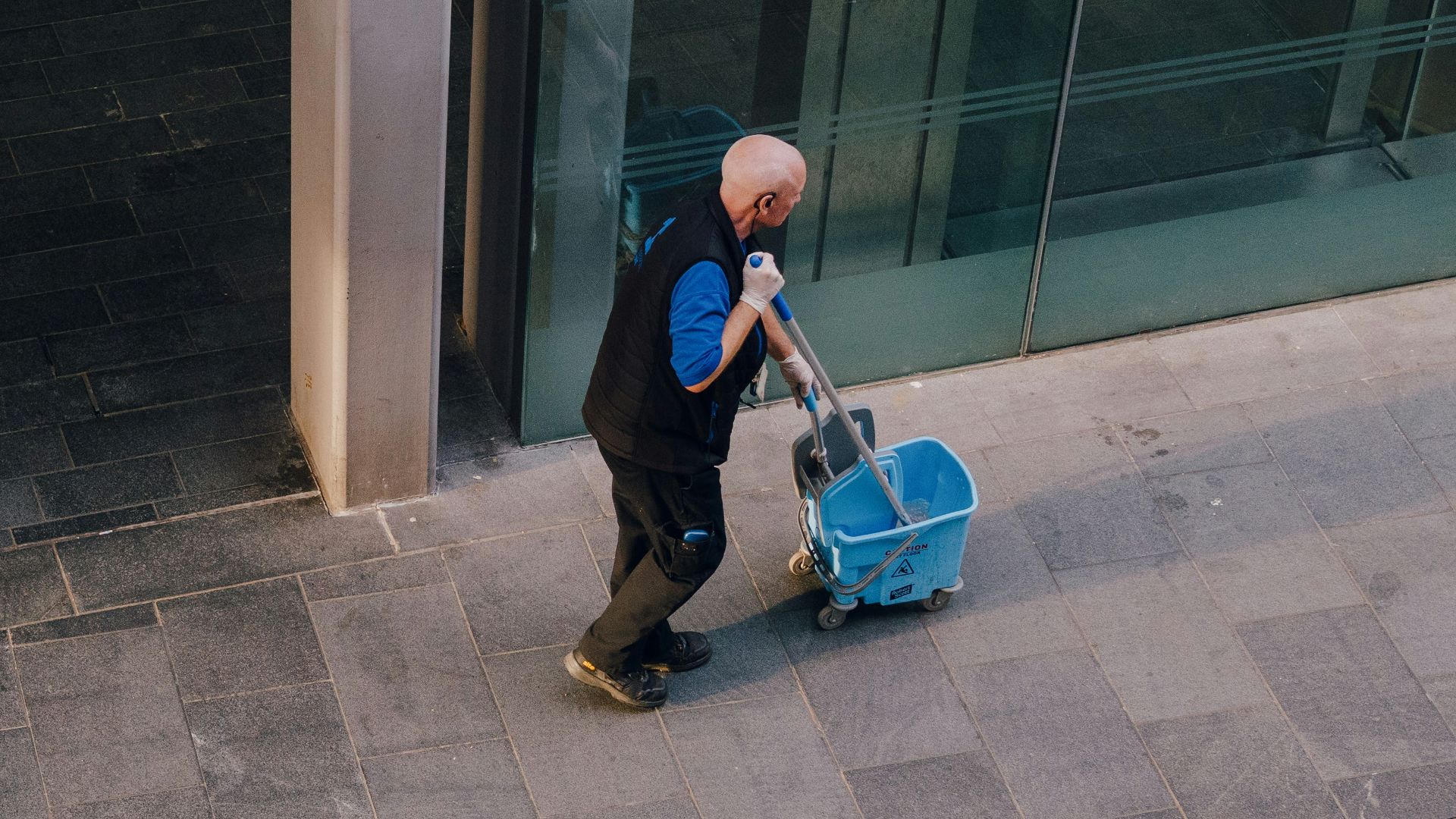 A man pulls a cleaning cart near a building.