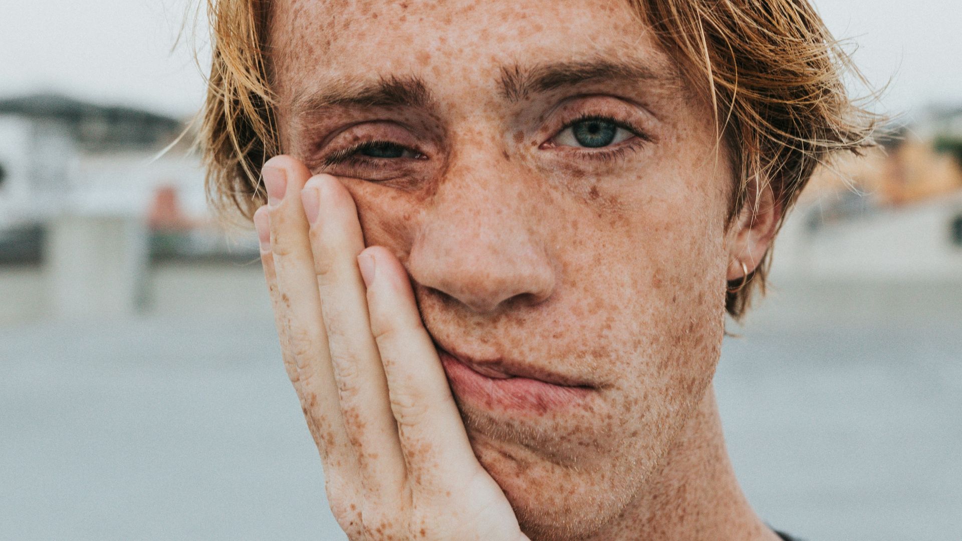 man in gray crew neck shirt with hand on face