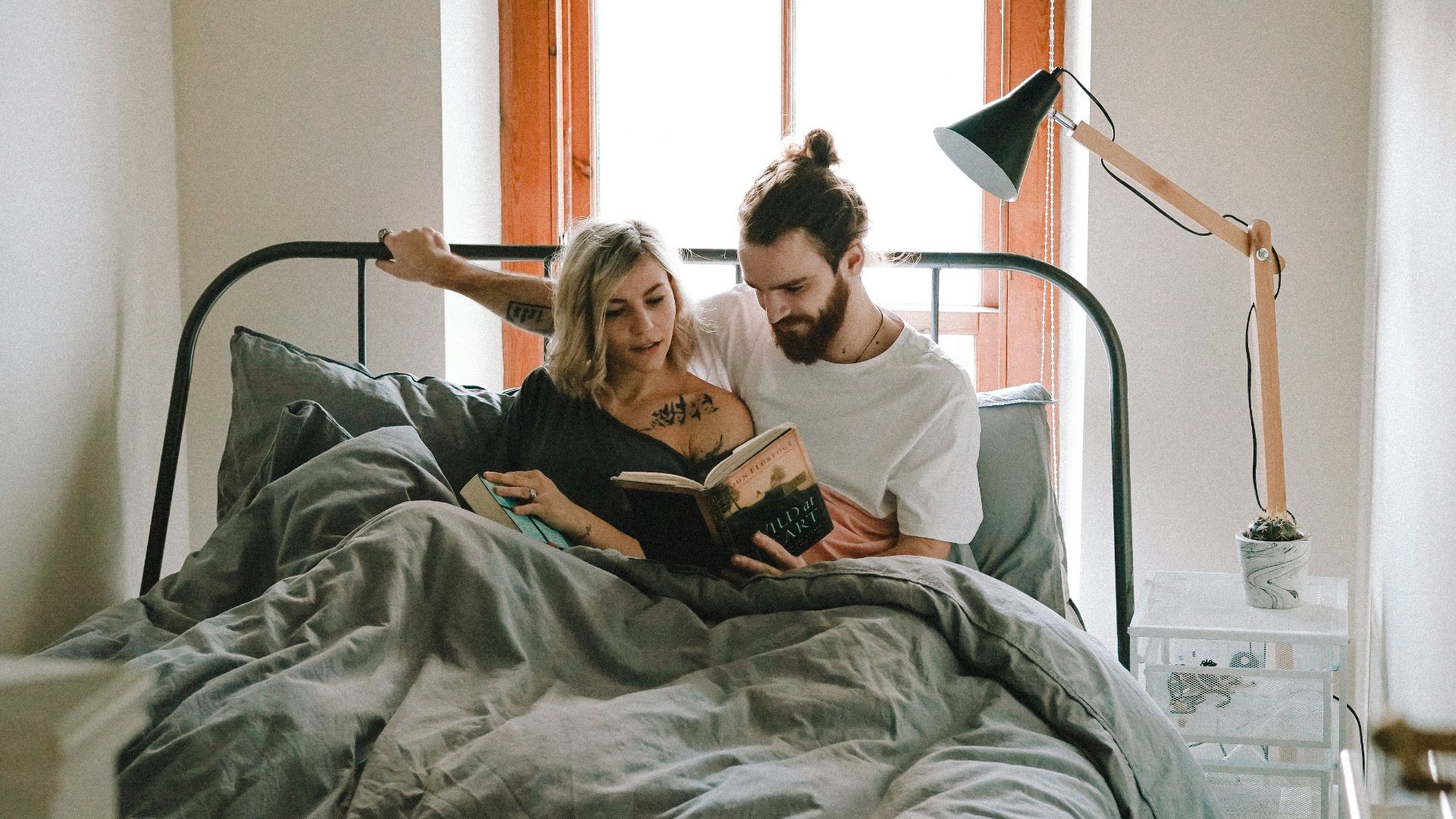 man and woman reading book on bed