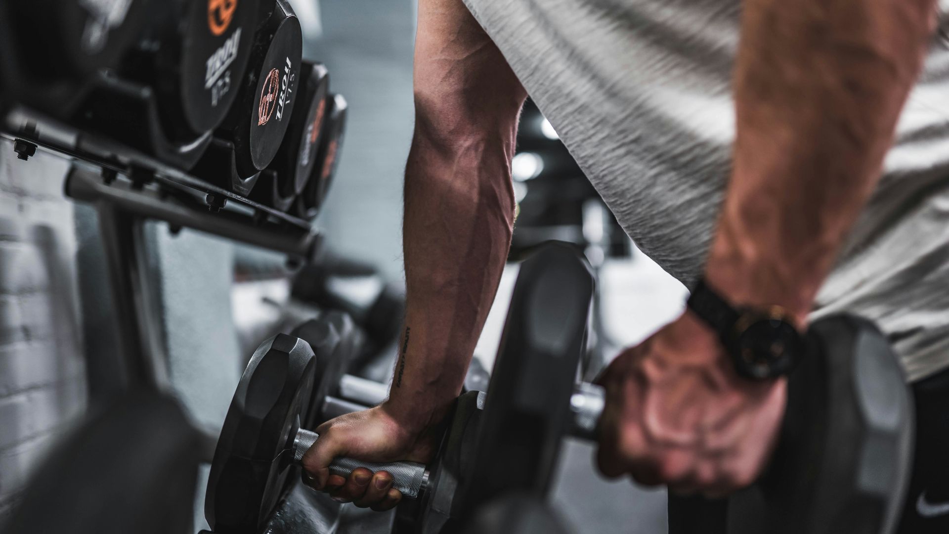 person in gray shirt holding black dumbbell