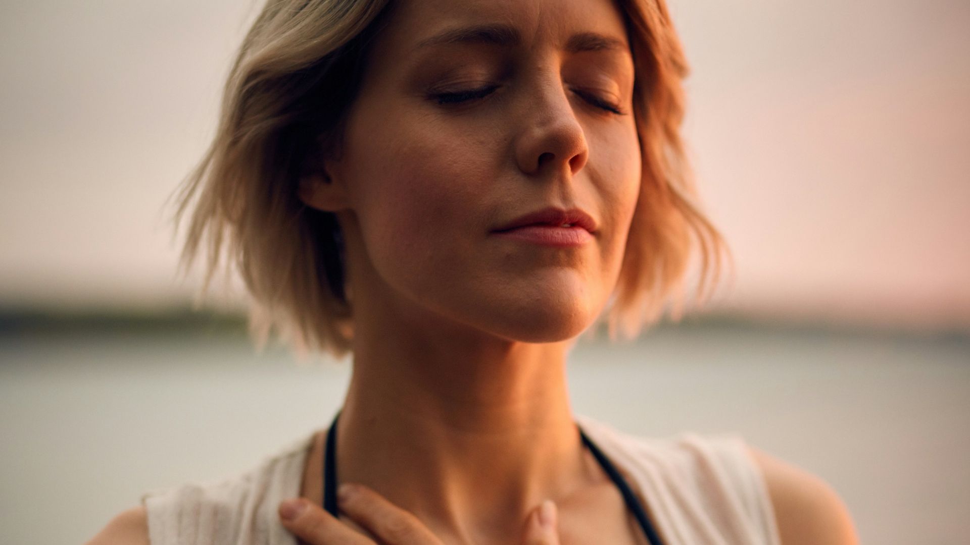 woman in white vest and black bikini with hand on chest