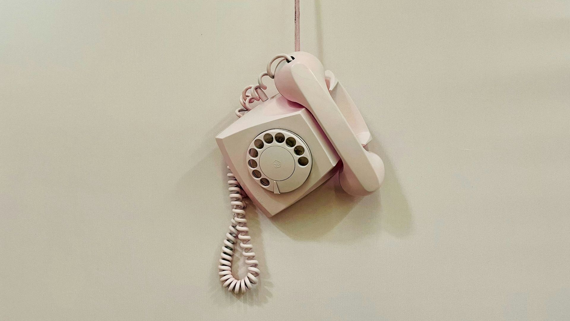 a pink phone hanging from a cord on a wall