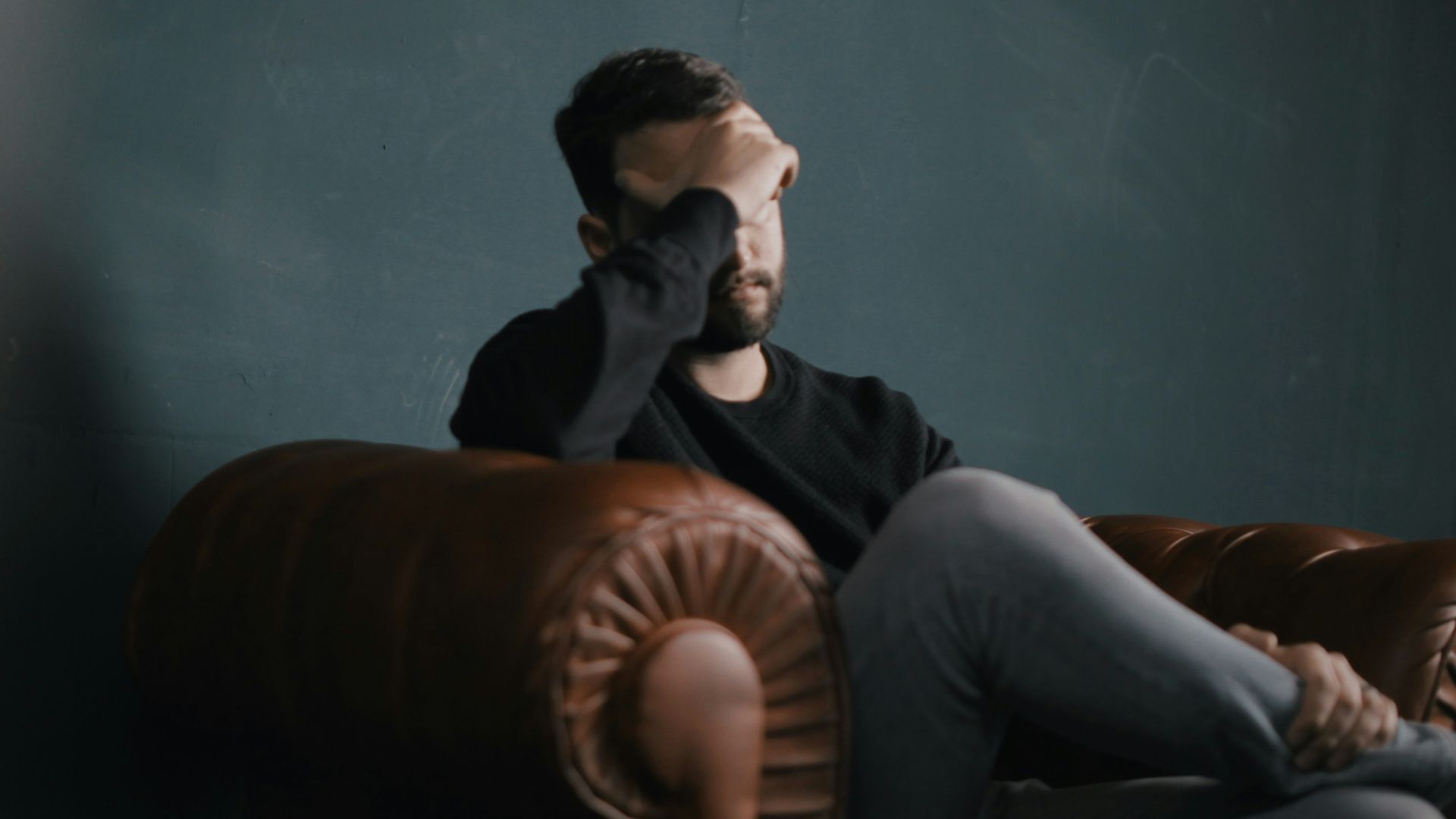 a man holds his head while sitting on a sofa
