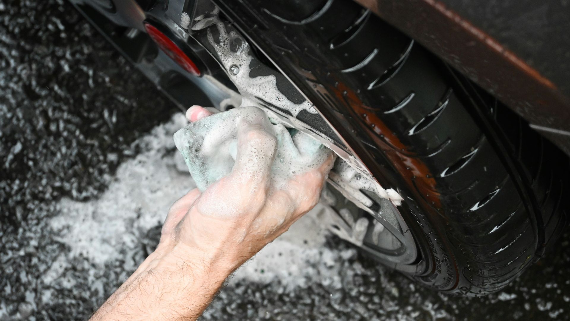 a man washing a car tire with a rag