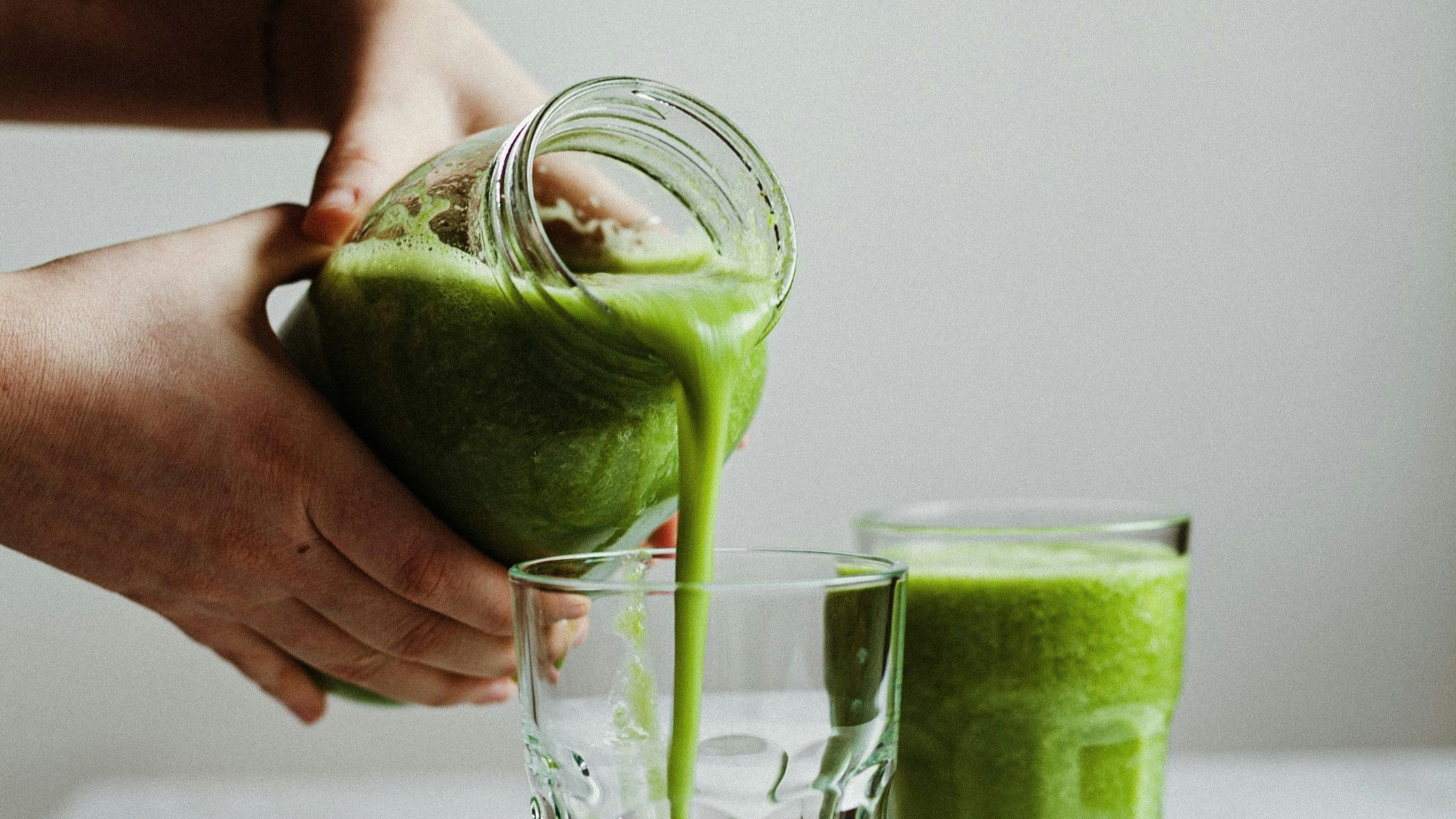 person holding clear drinking glass with green liquid