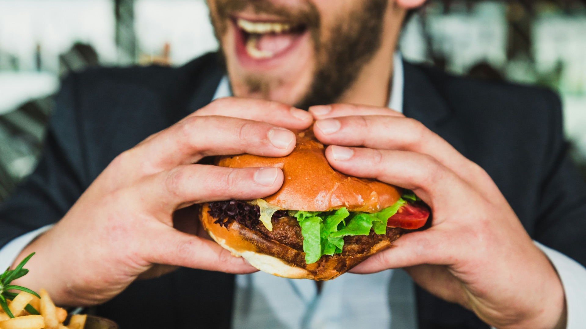 person holding burger bun with vegetables and meat