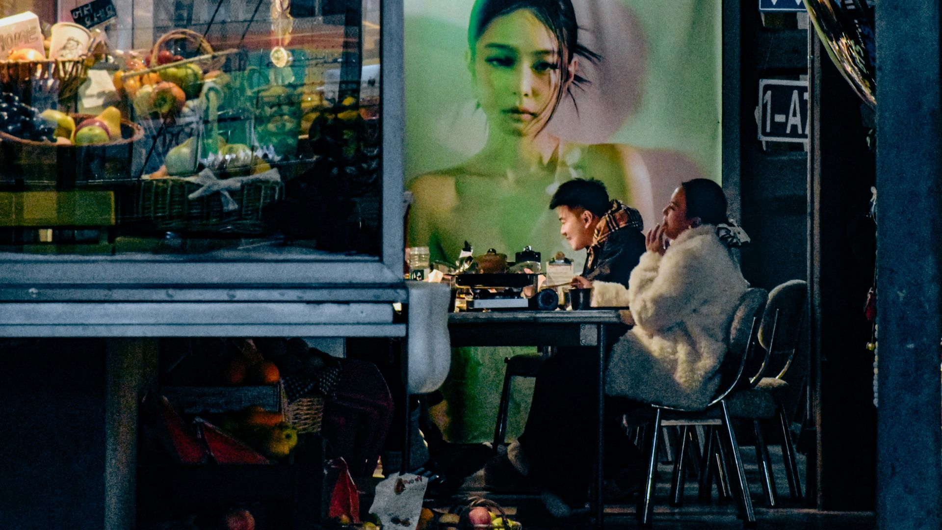 People sit at a table outside a shop with advertisement.