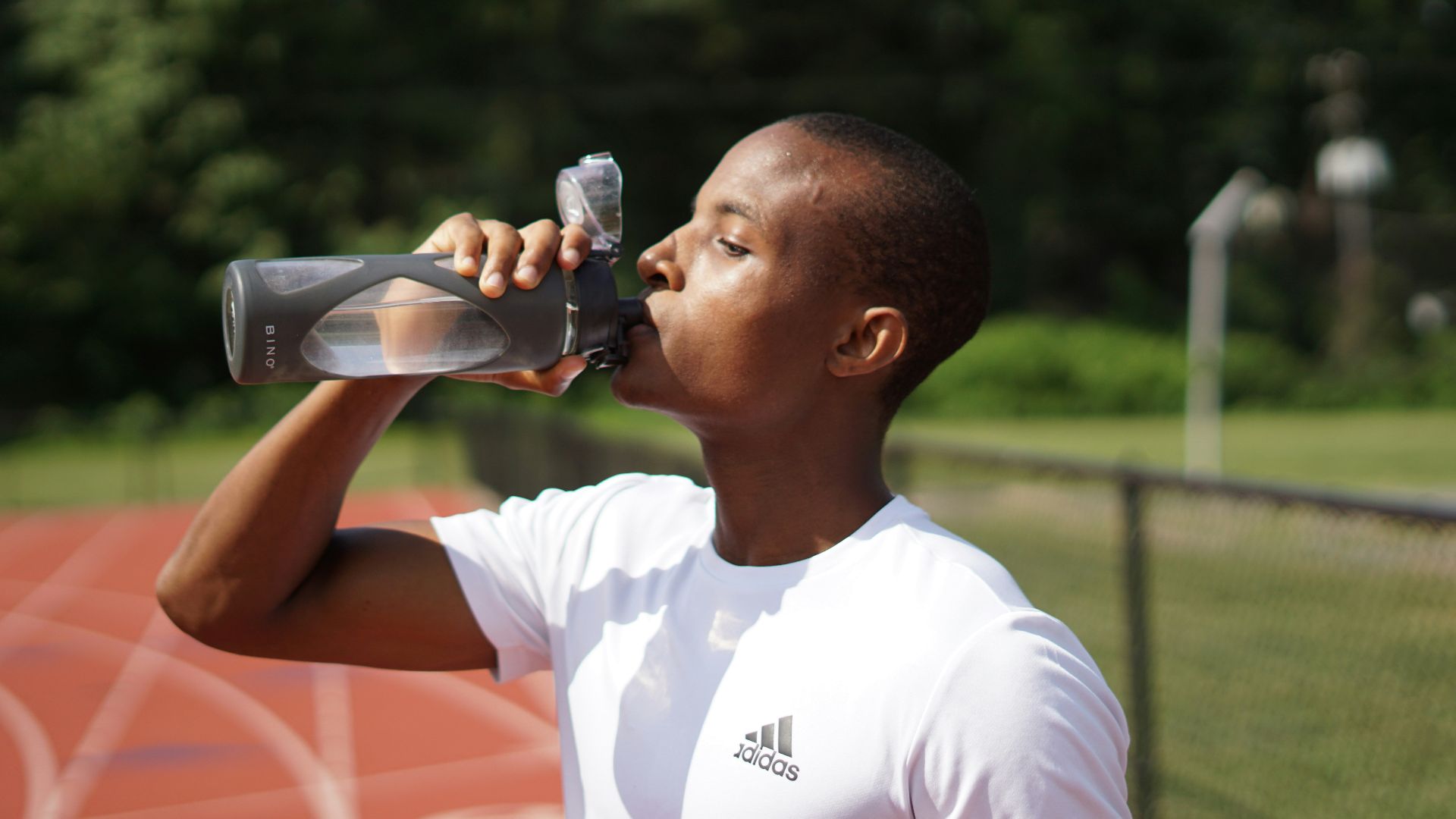 man in white crew neck t-shirt drinking from black sports bottle