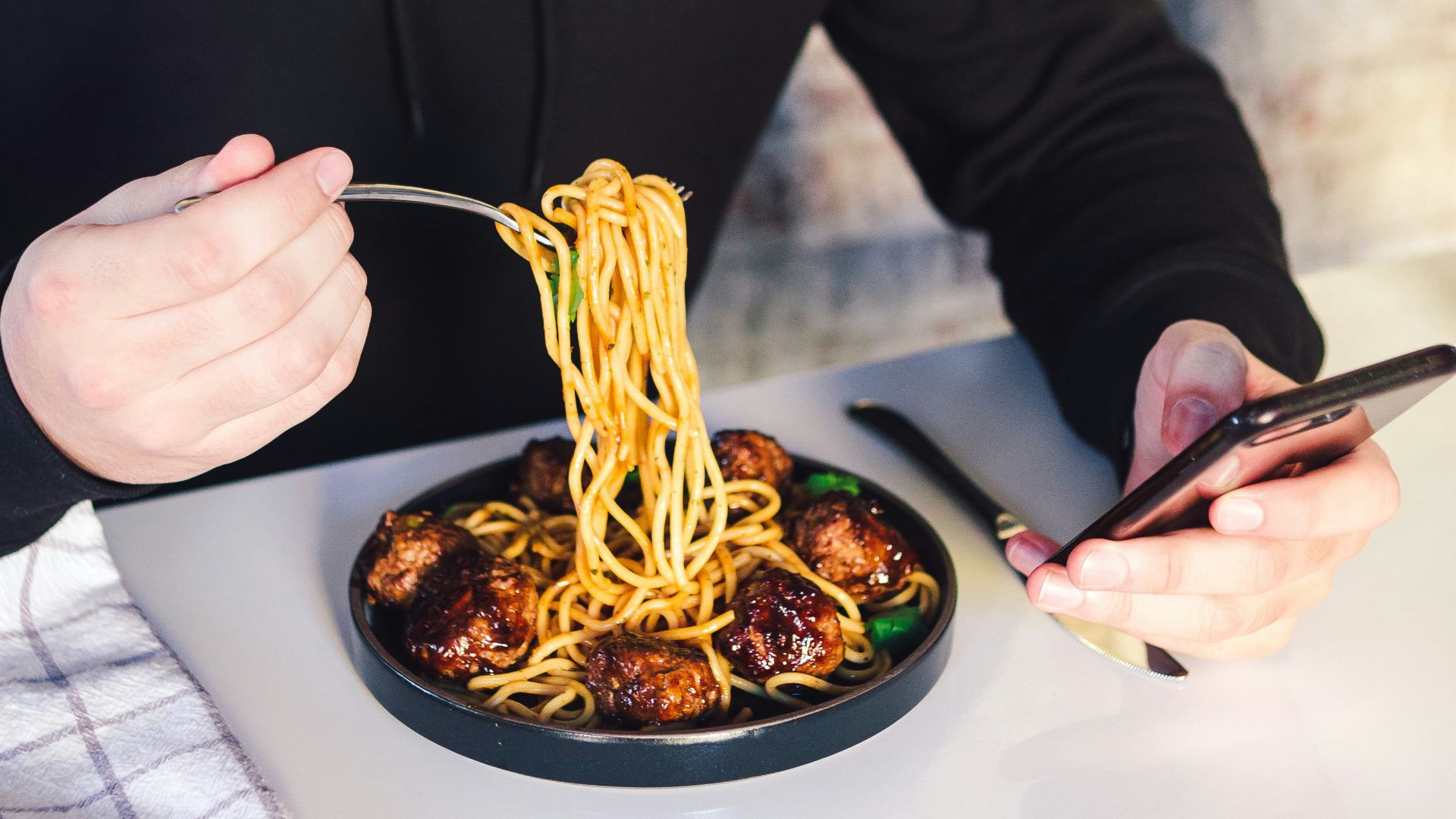 man eating cooked noodle while using phone