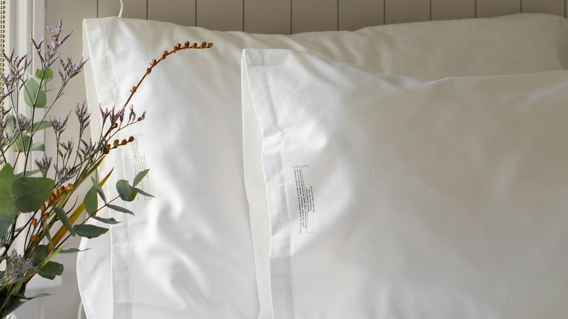 a bed with white sheets and pillows and a vase with flowers