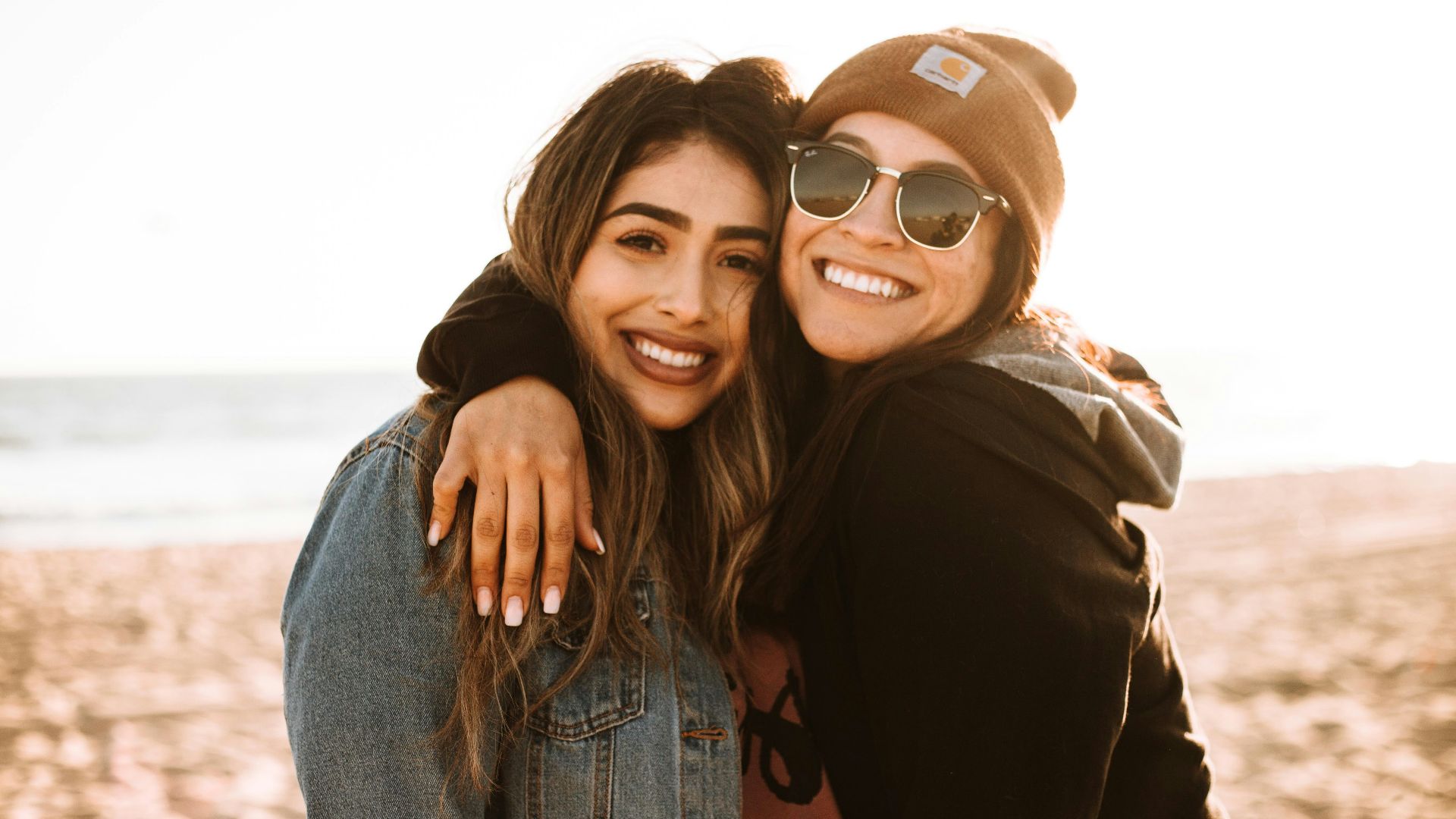 woman hugging other woman while smiling at beach
