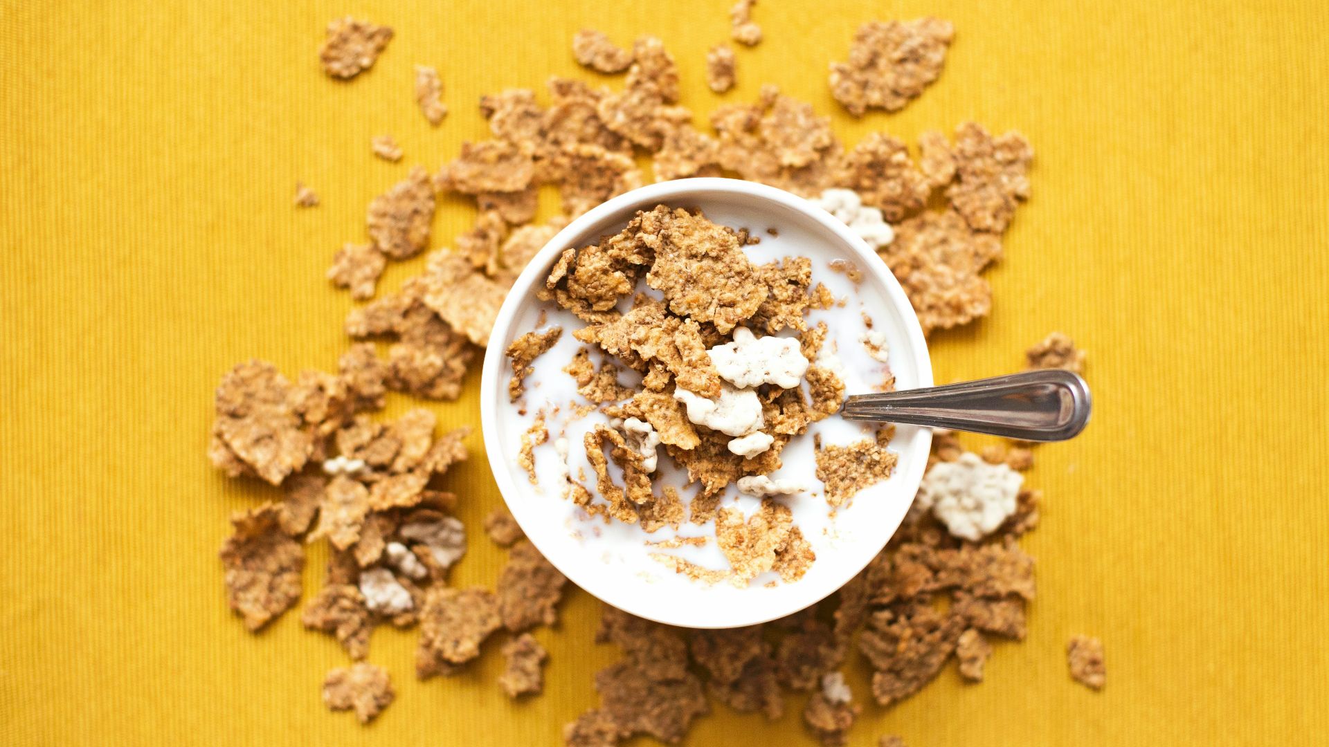 top view of corn flakes in bowl with milk and silver spoon