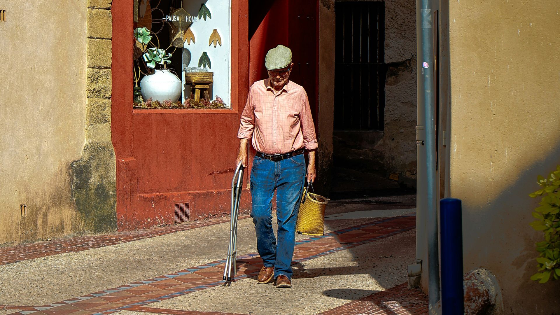 Man walks down a narrow street with a cane.