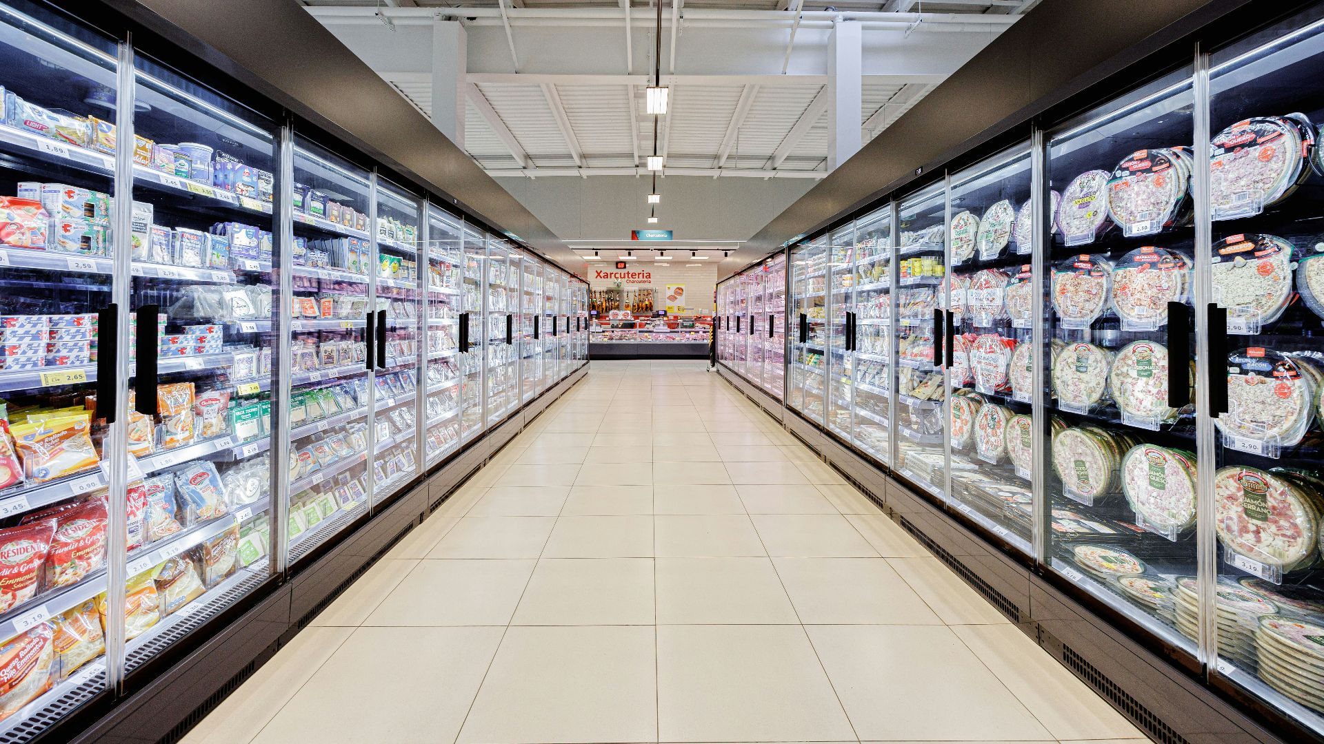 A long aisle in a brightly lit supermarket with refrigerators.