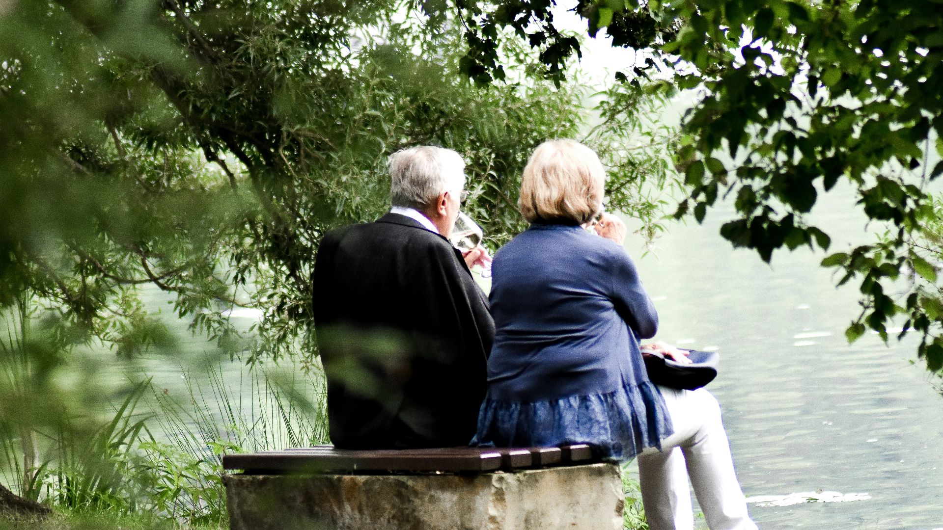 two people sitting on pavement facing on body of water