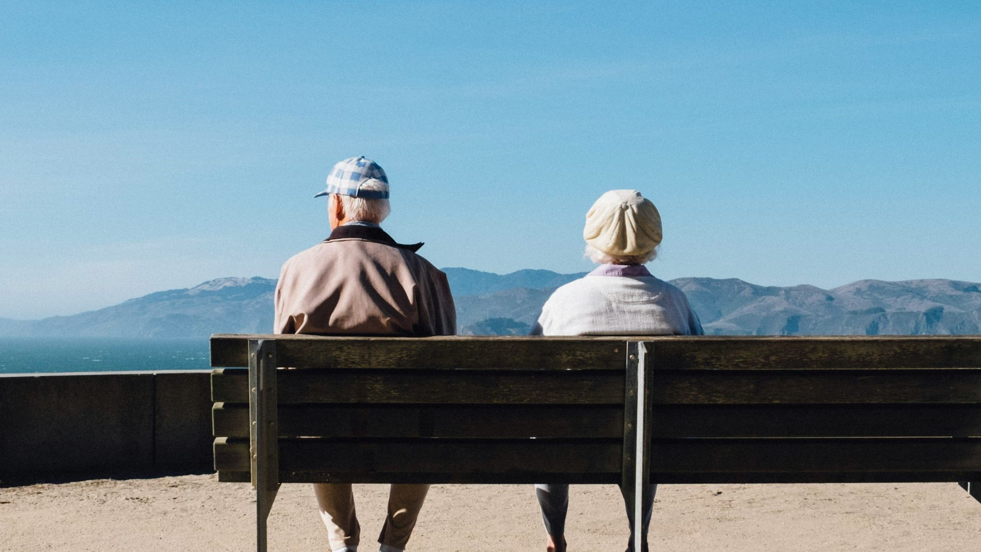 man and woman sitting on bench facing sea