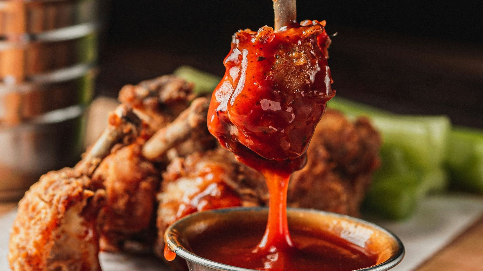 Hand dipping chicken wing in barbecue sauce