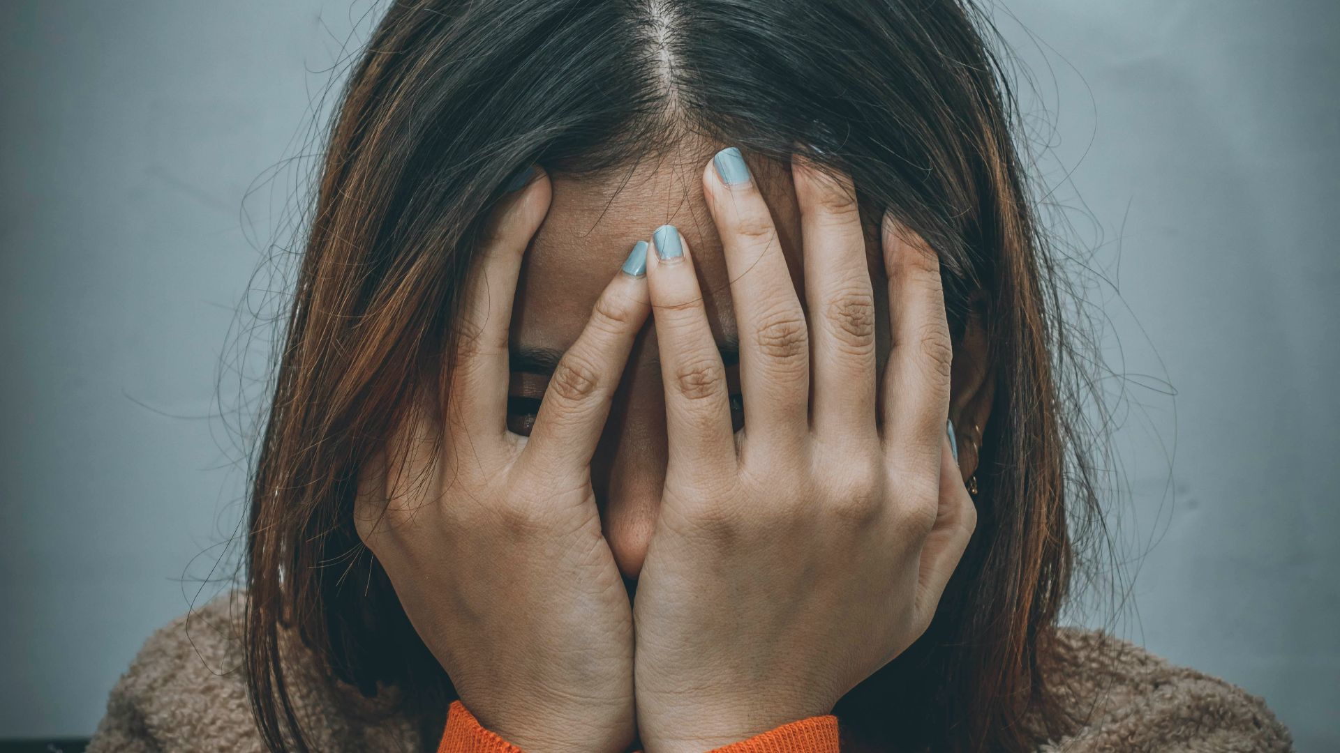 woman in brown sweater covering her face with her hand