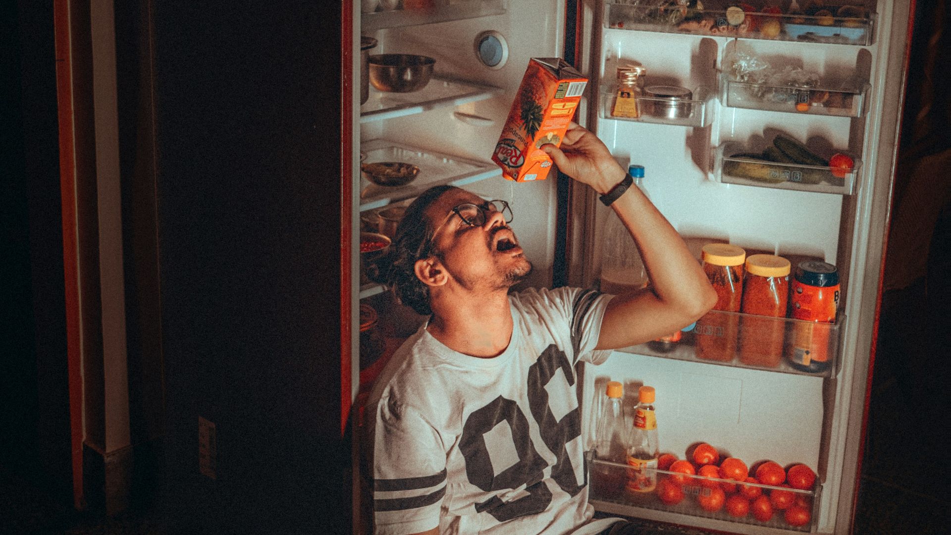 boy in white and black tank top standing beside red top mount refrigerator