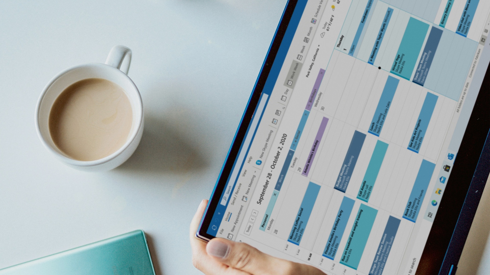 person holding ipad near white ceramic mug and laptop
