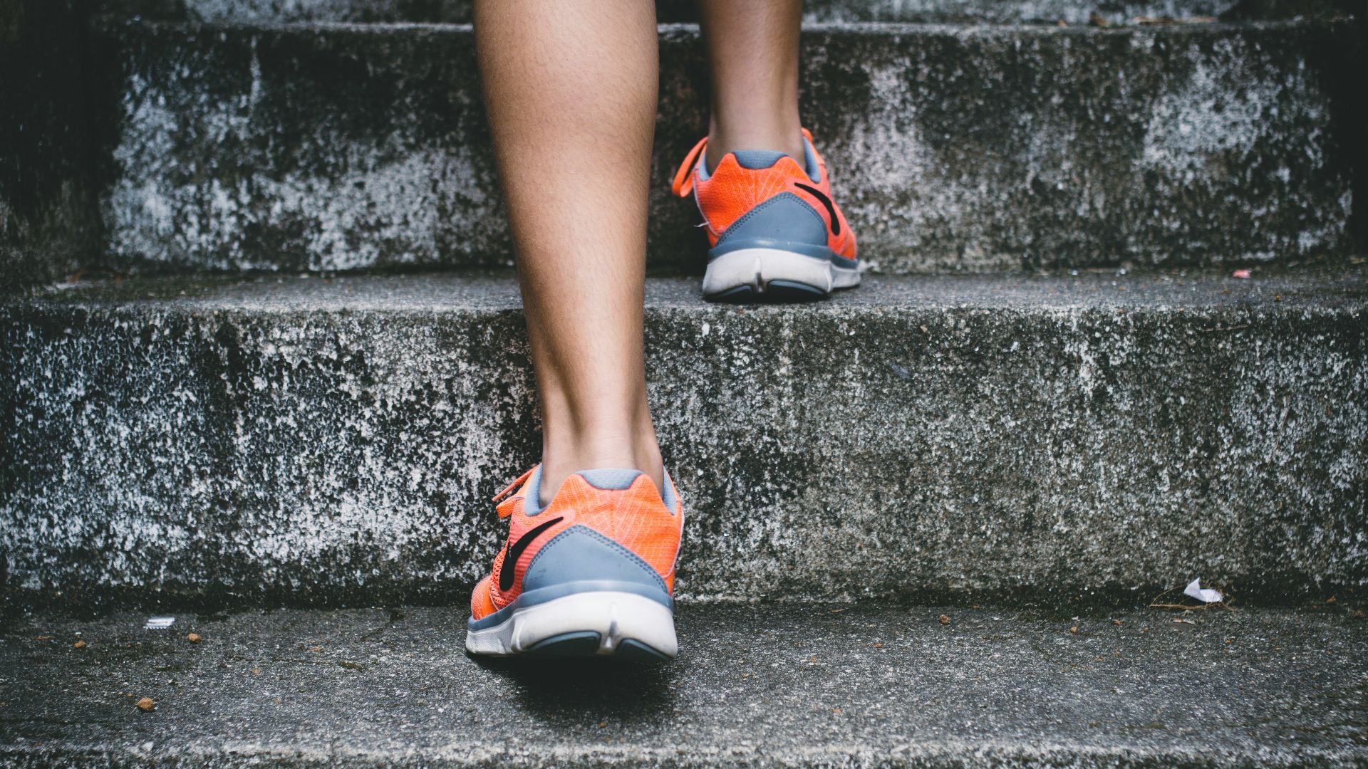 person wearing orange and gray Nike shoes walking on gray concrete stairs