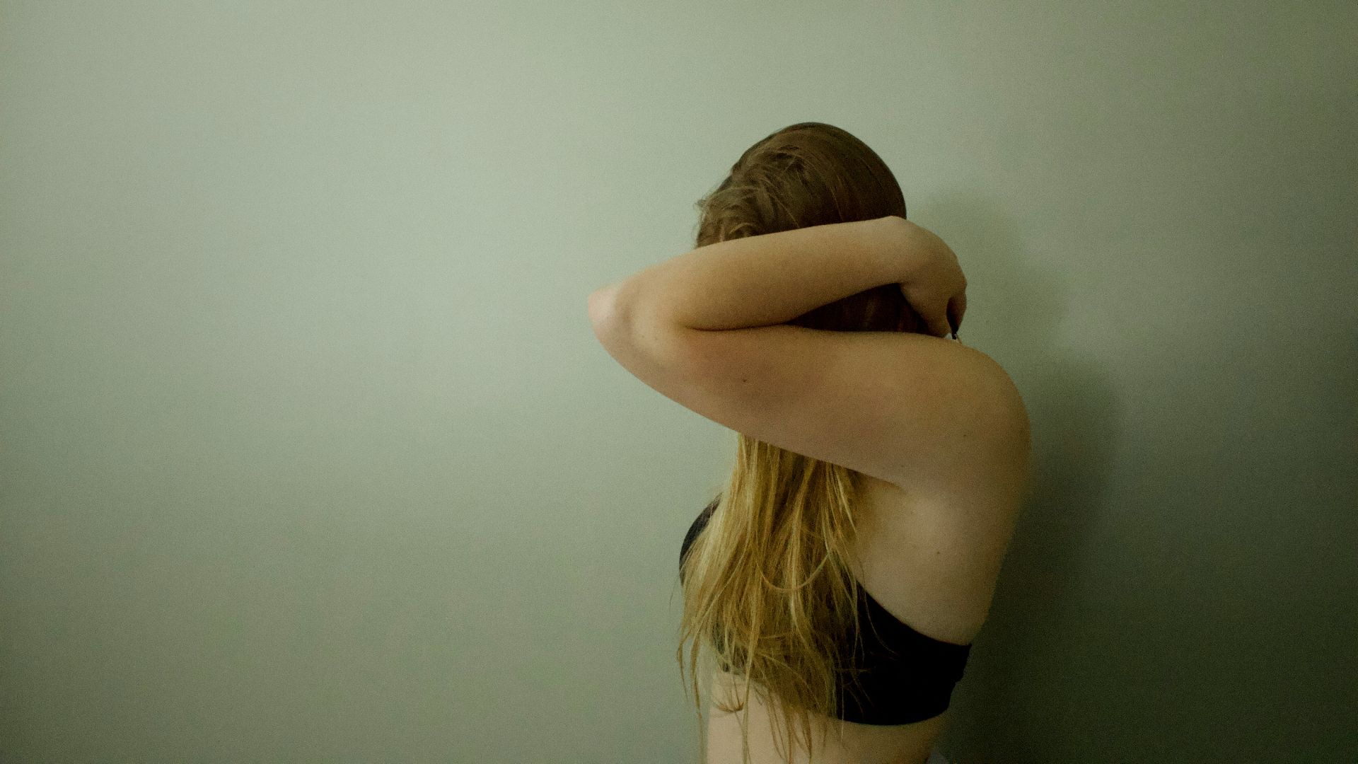 a woman with her head in her hands leaning against a wall