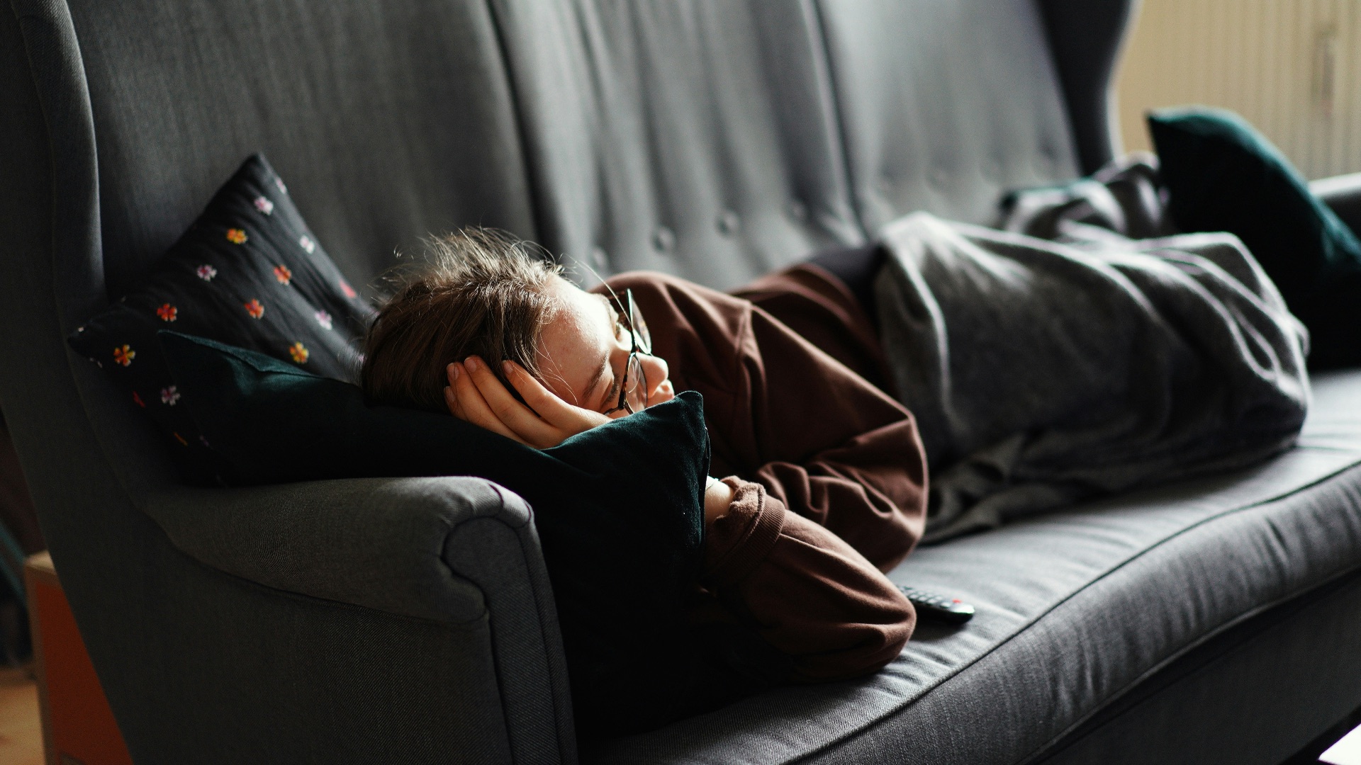 woman in pink jacket lying on gray couch
